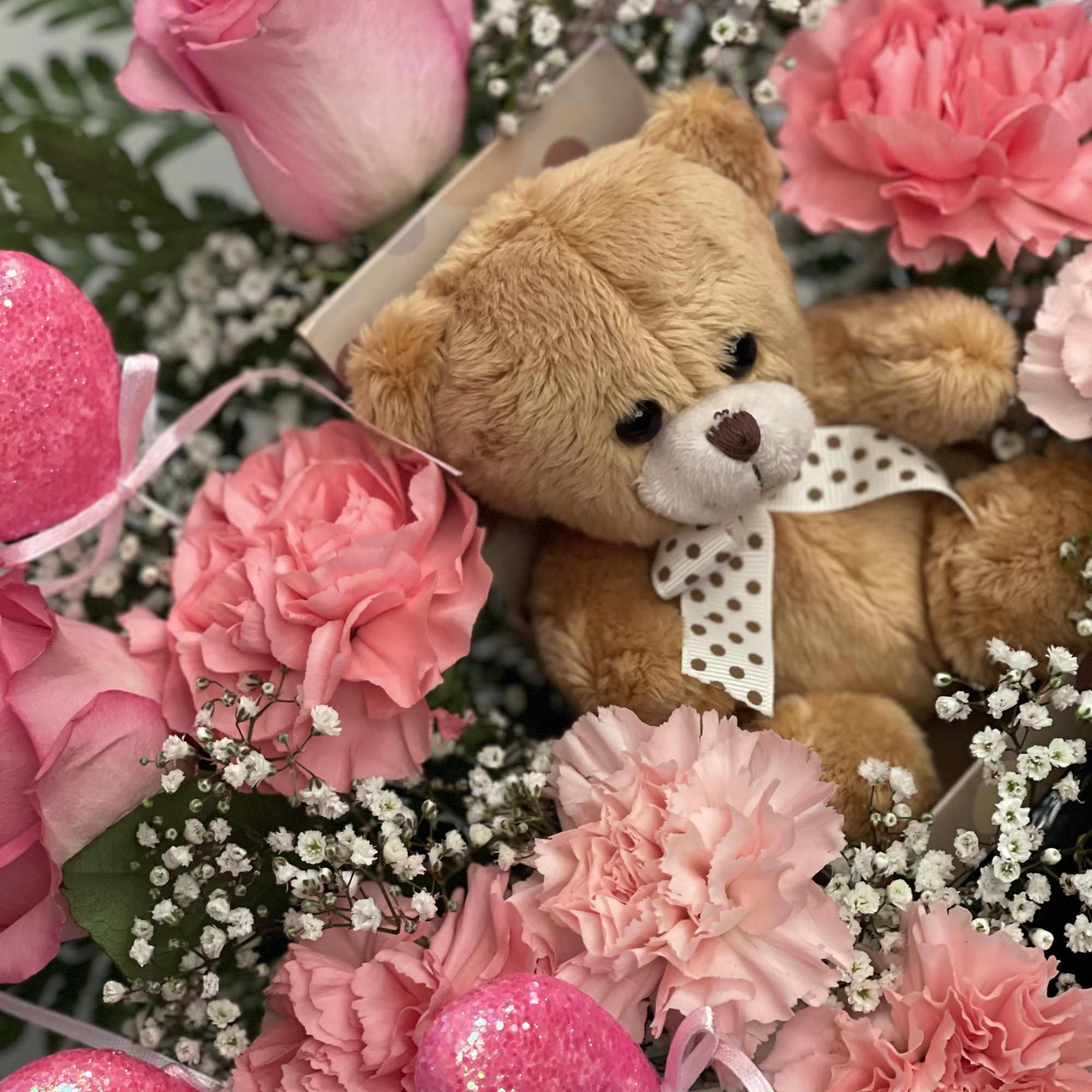 Pink flowers arranged around a teddy bear and glittery heart decorations
