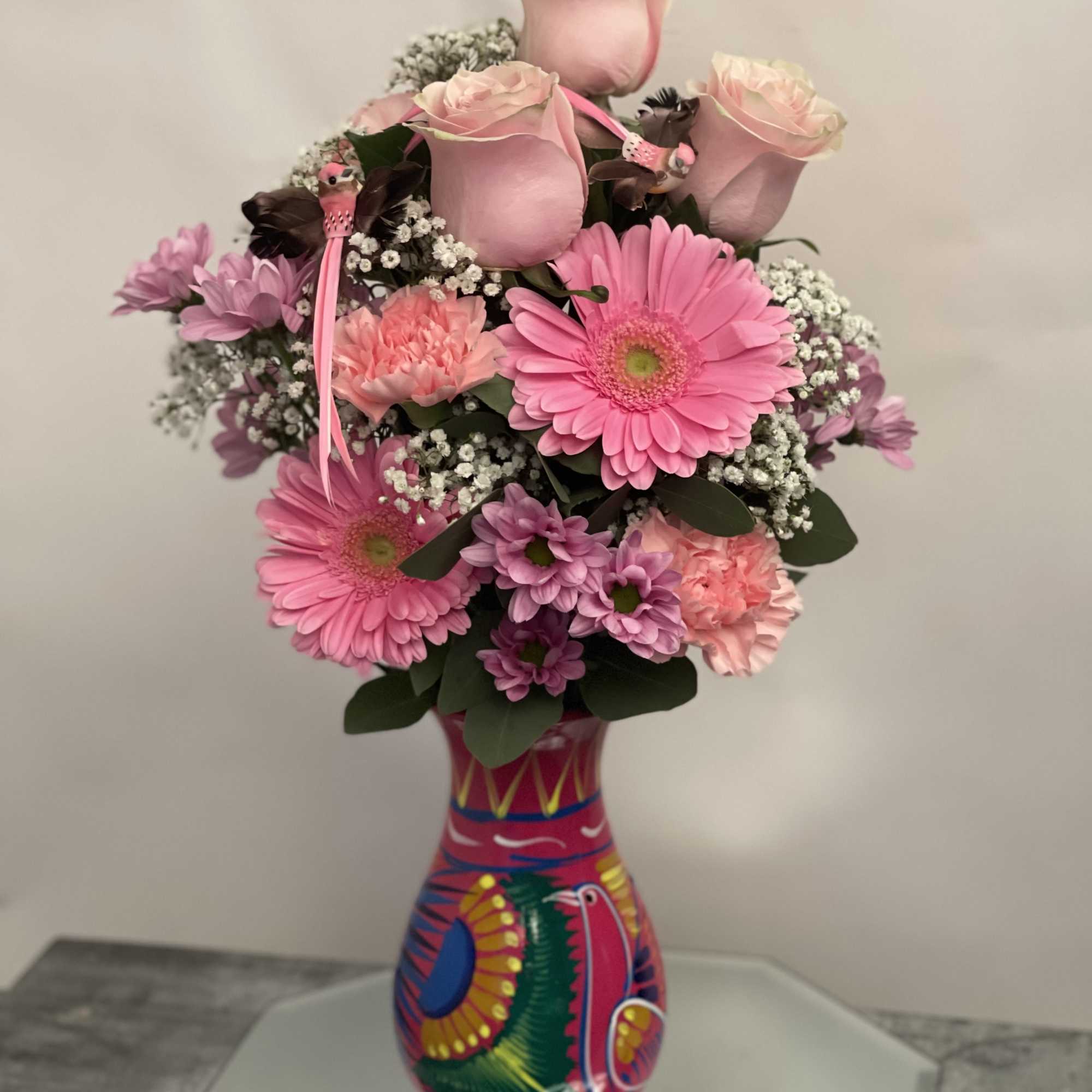 Pink roses and gerbera daisies arranged in a colorful painted vase