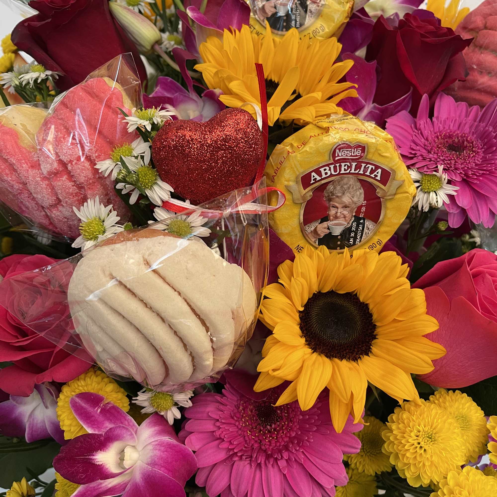 Bright mixed bouquet with sunflowers, roses, orchids, and packaged cookies