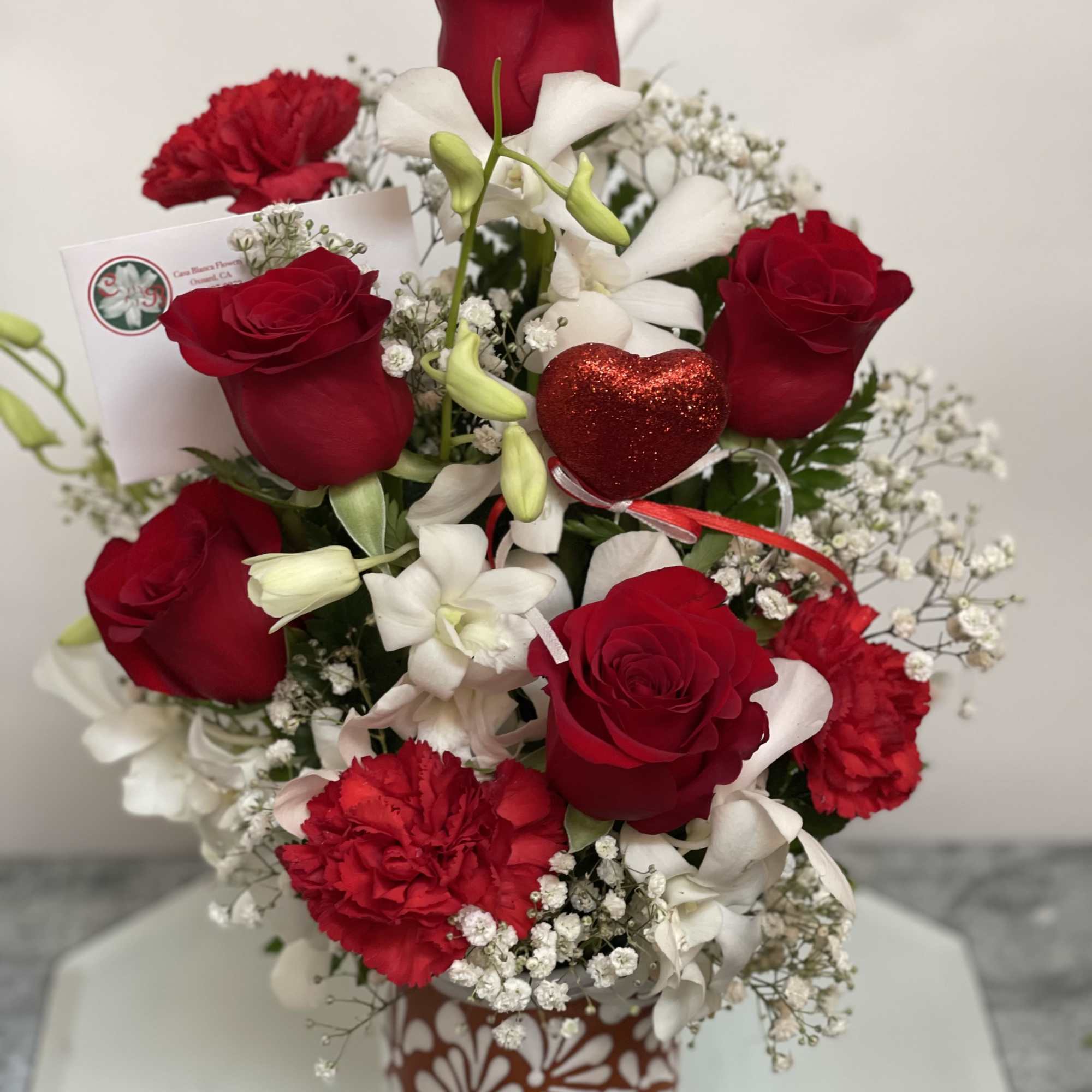 Red roses and white orchids in a decorative vase with a glittery heart pick