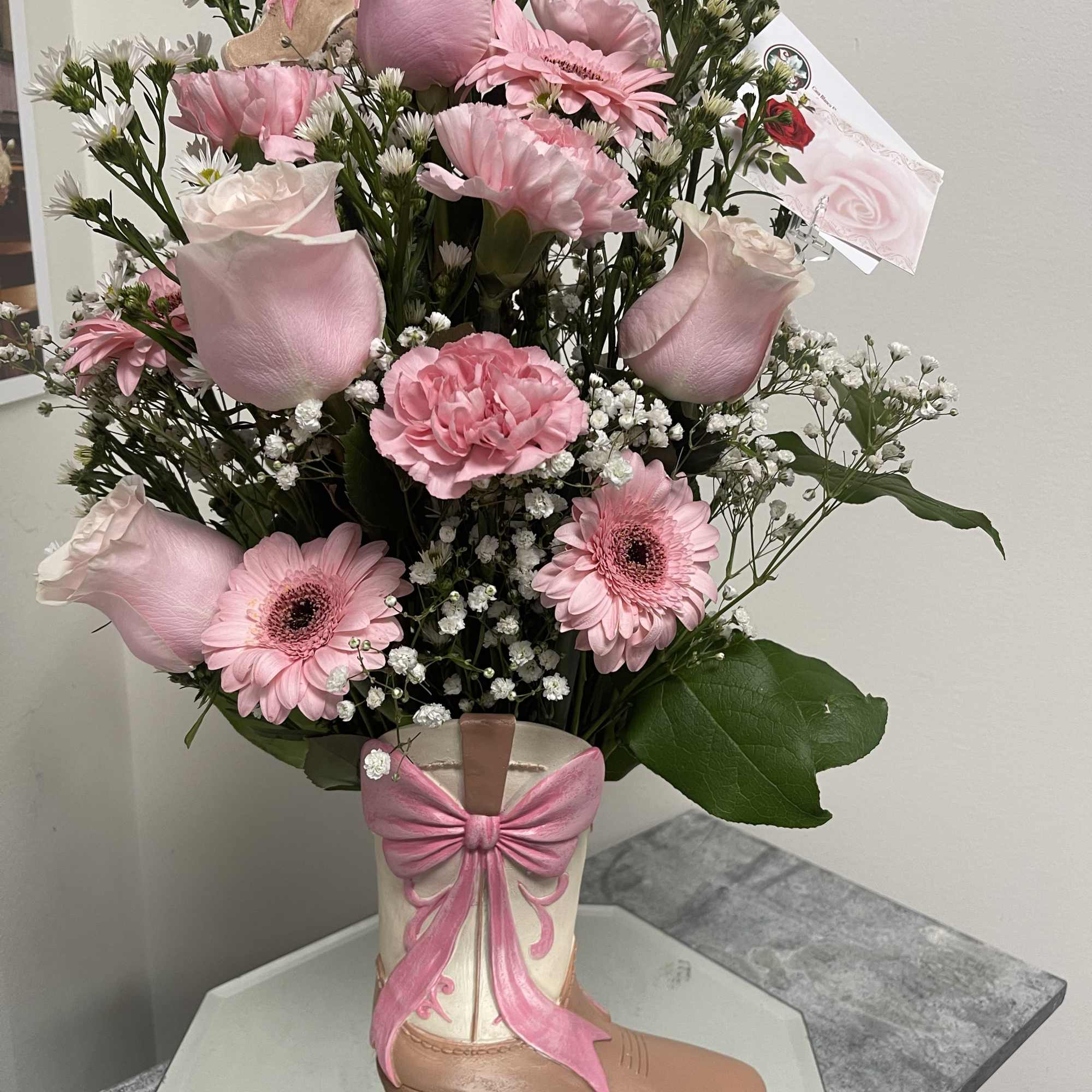 Pink floral arrangement in a decorative boot vase with a bow