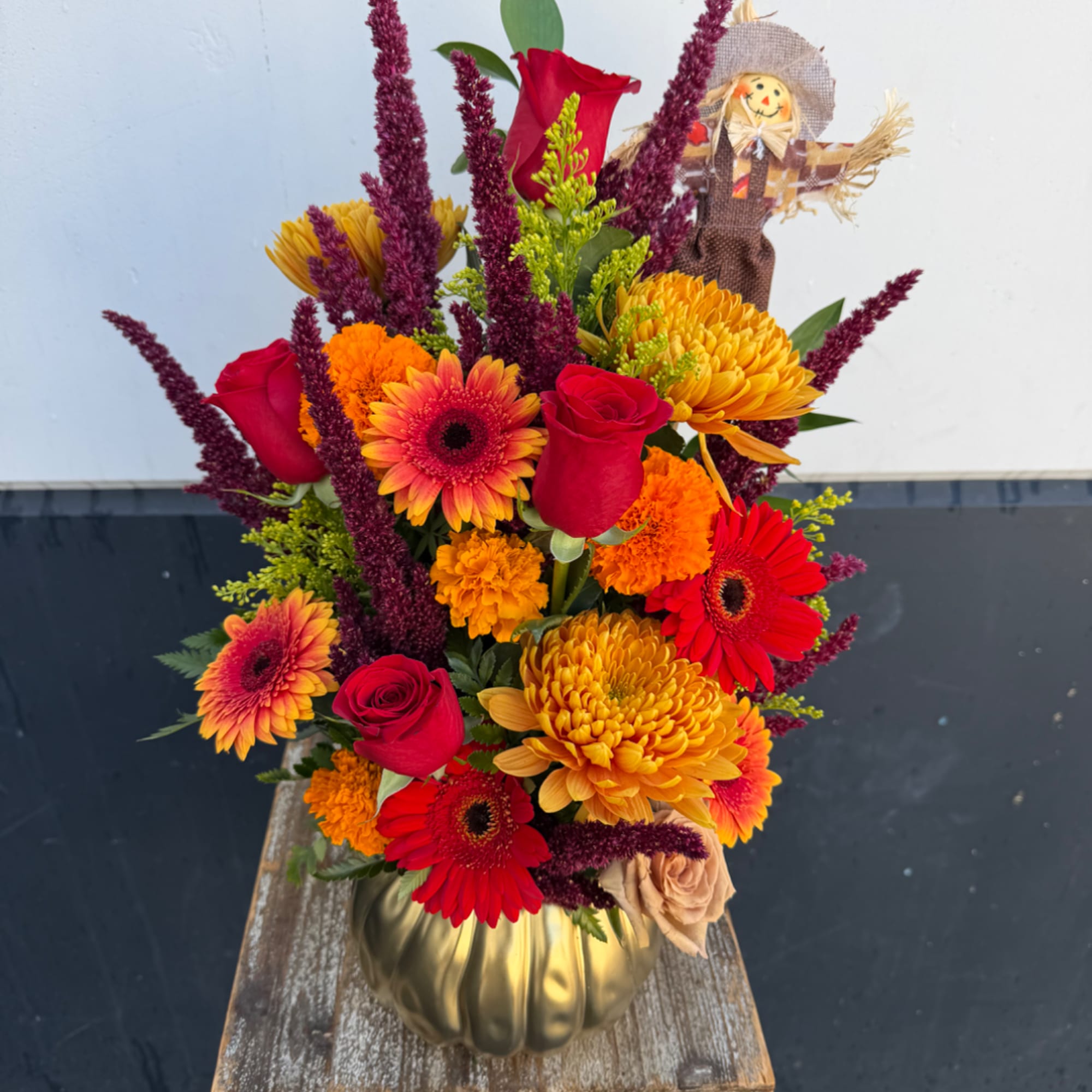 Bright mixed bouquet in a gold vase with a small scarecrow pick