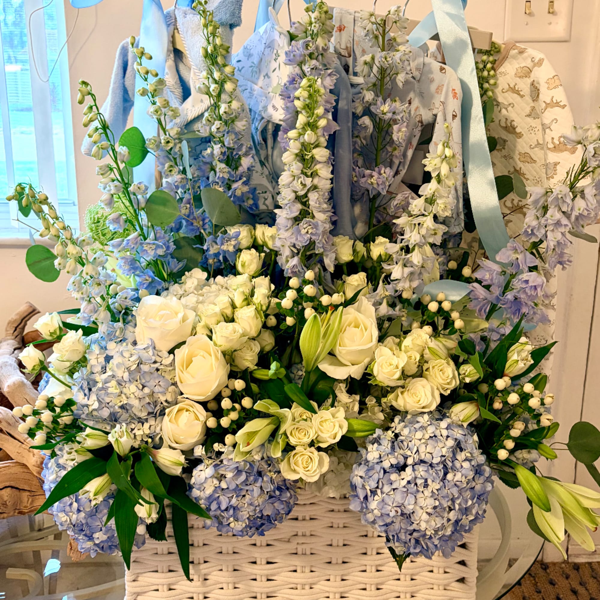 Blue and white floral arrangement in a white basket with ribbon handles