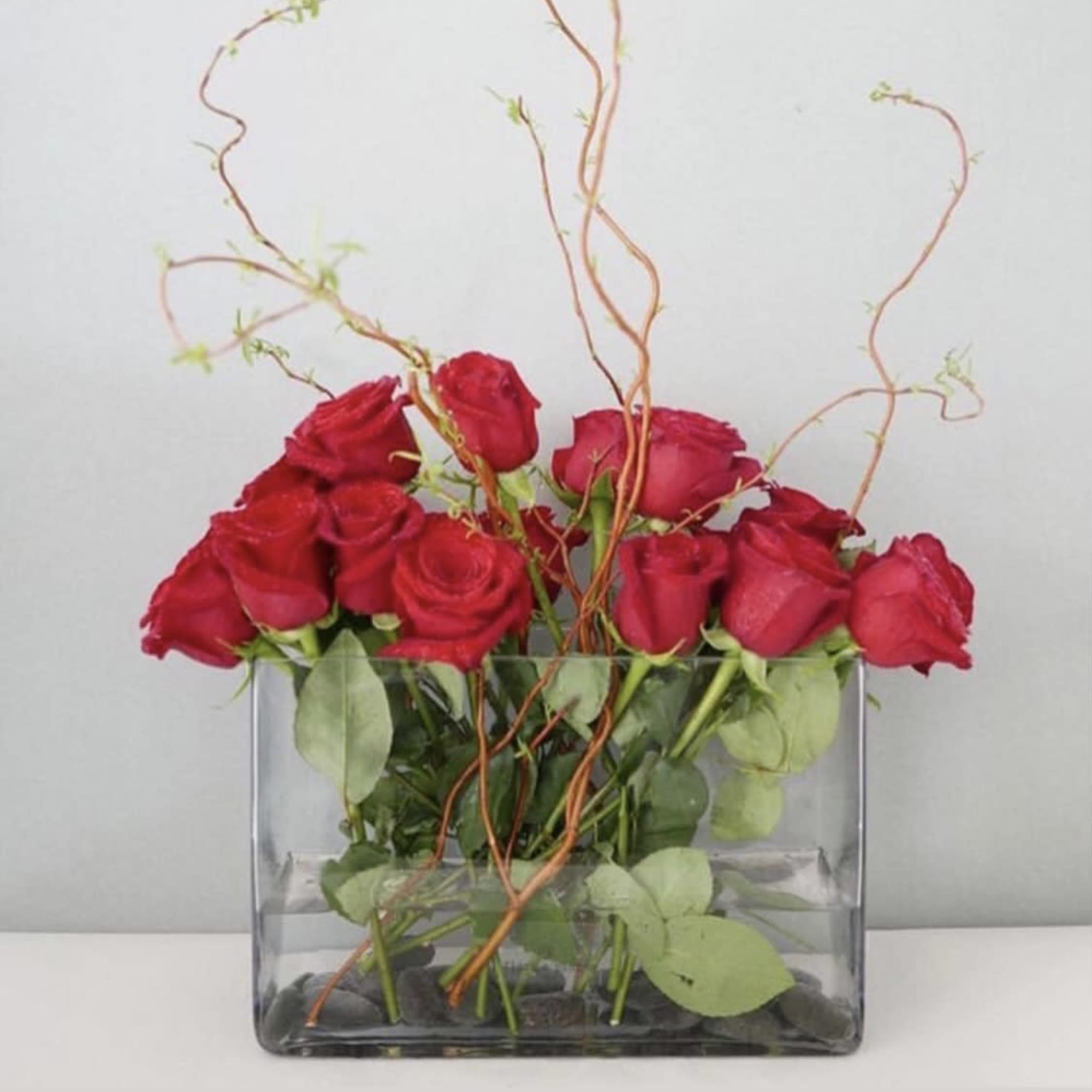 Red roses arranged in a clear rectangular vase with curly branches