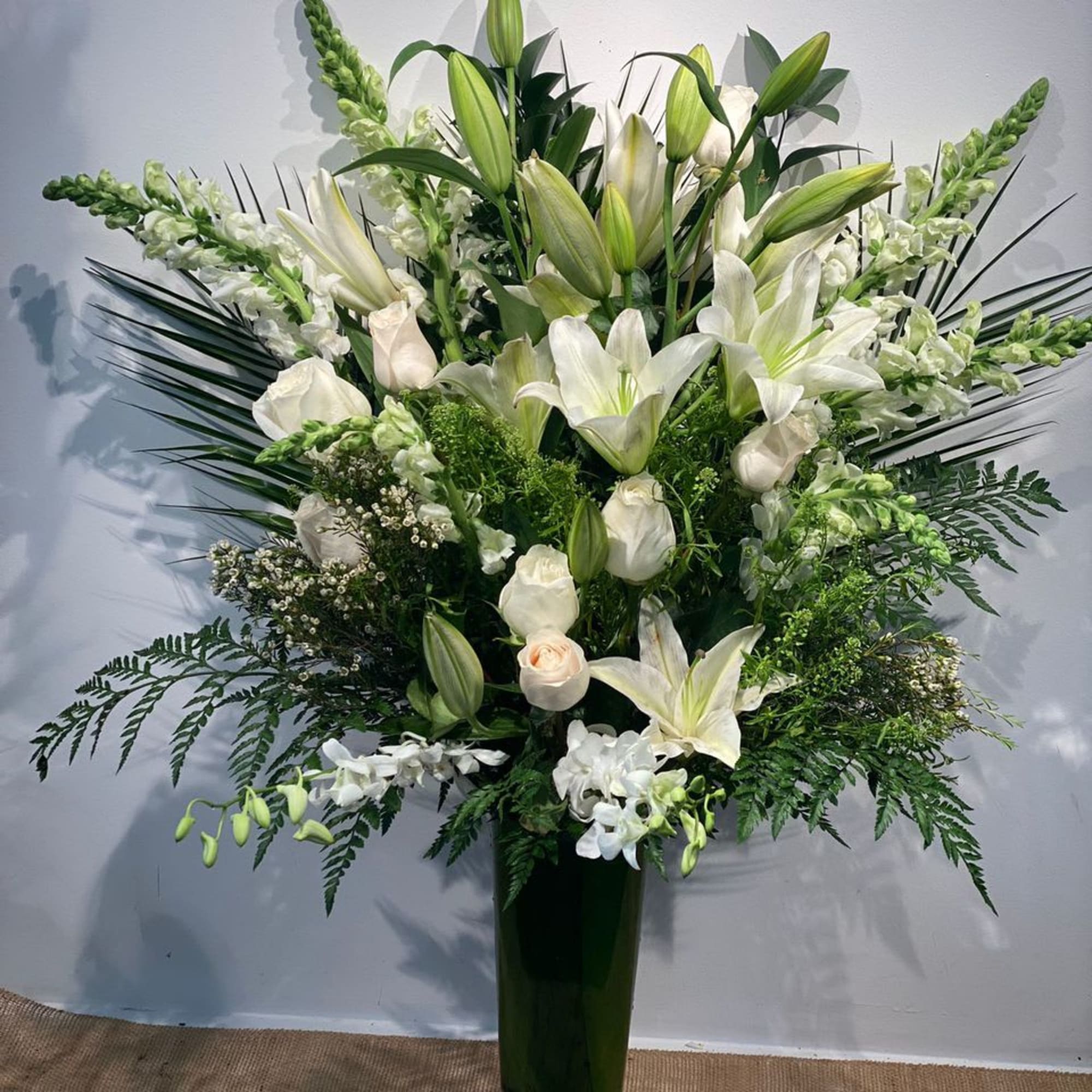 Tall white lily and rose arrangement in a dark glass vase