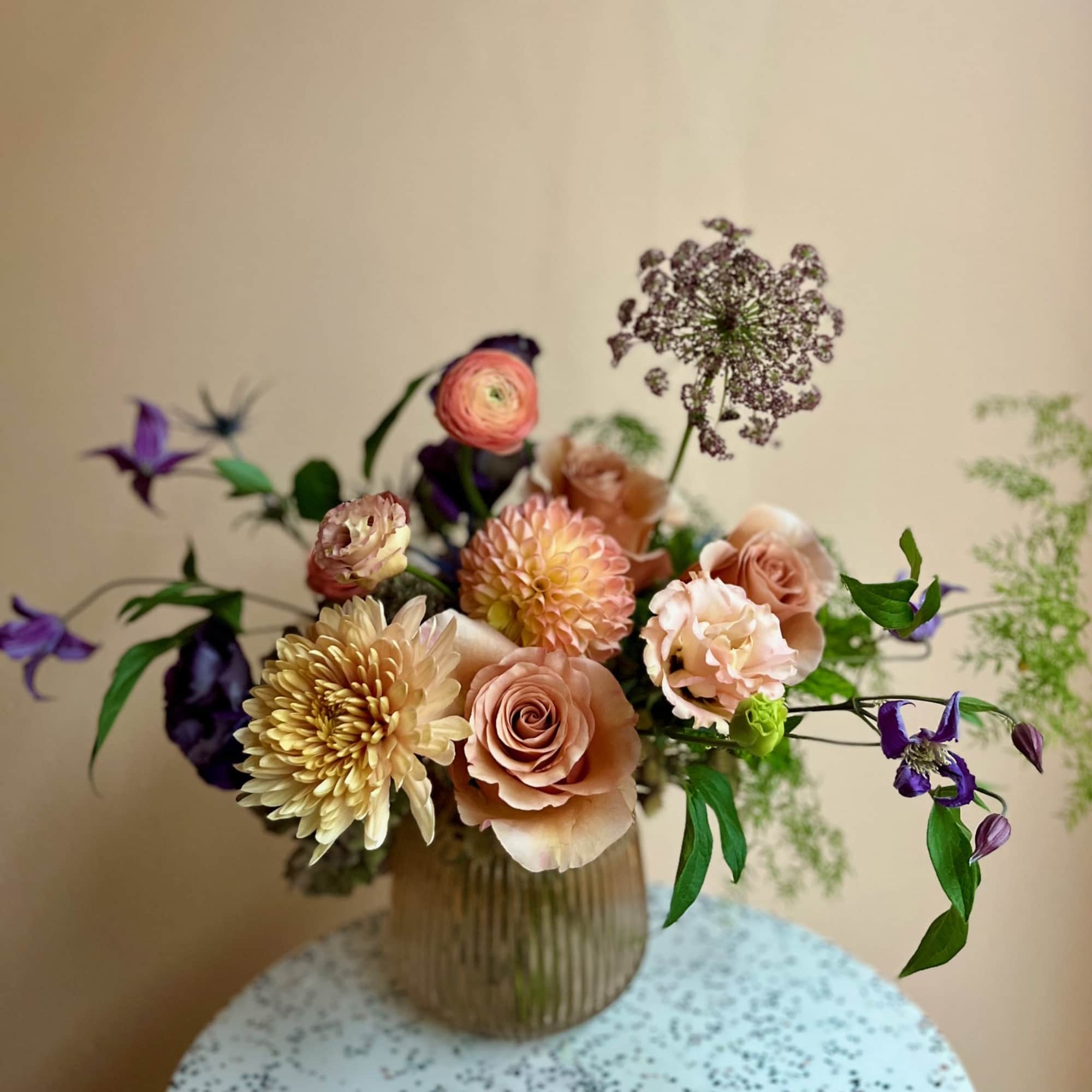 Peach and cream bouquet in a ribbed glass vase with purple accents
