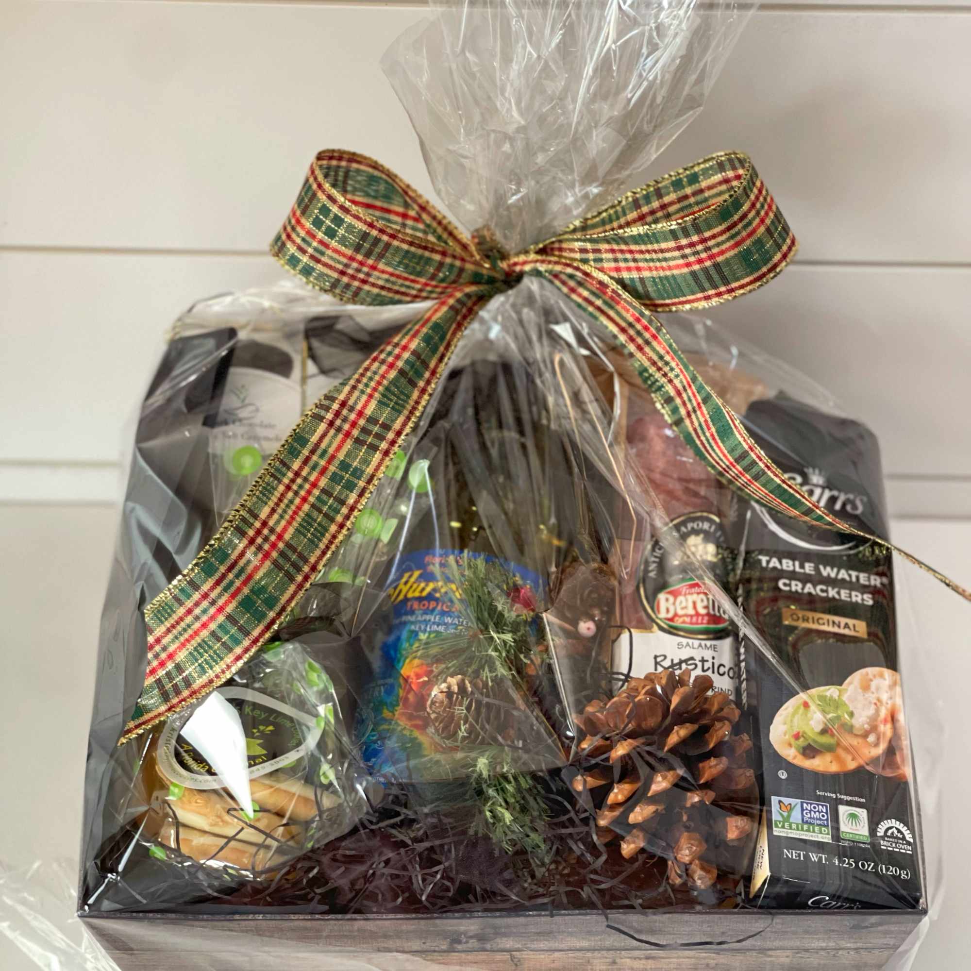 Gift basket with crackers, salami, and other packaged snacks tied with a plaid ribbon