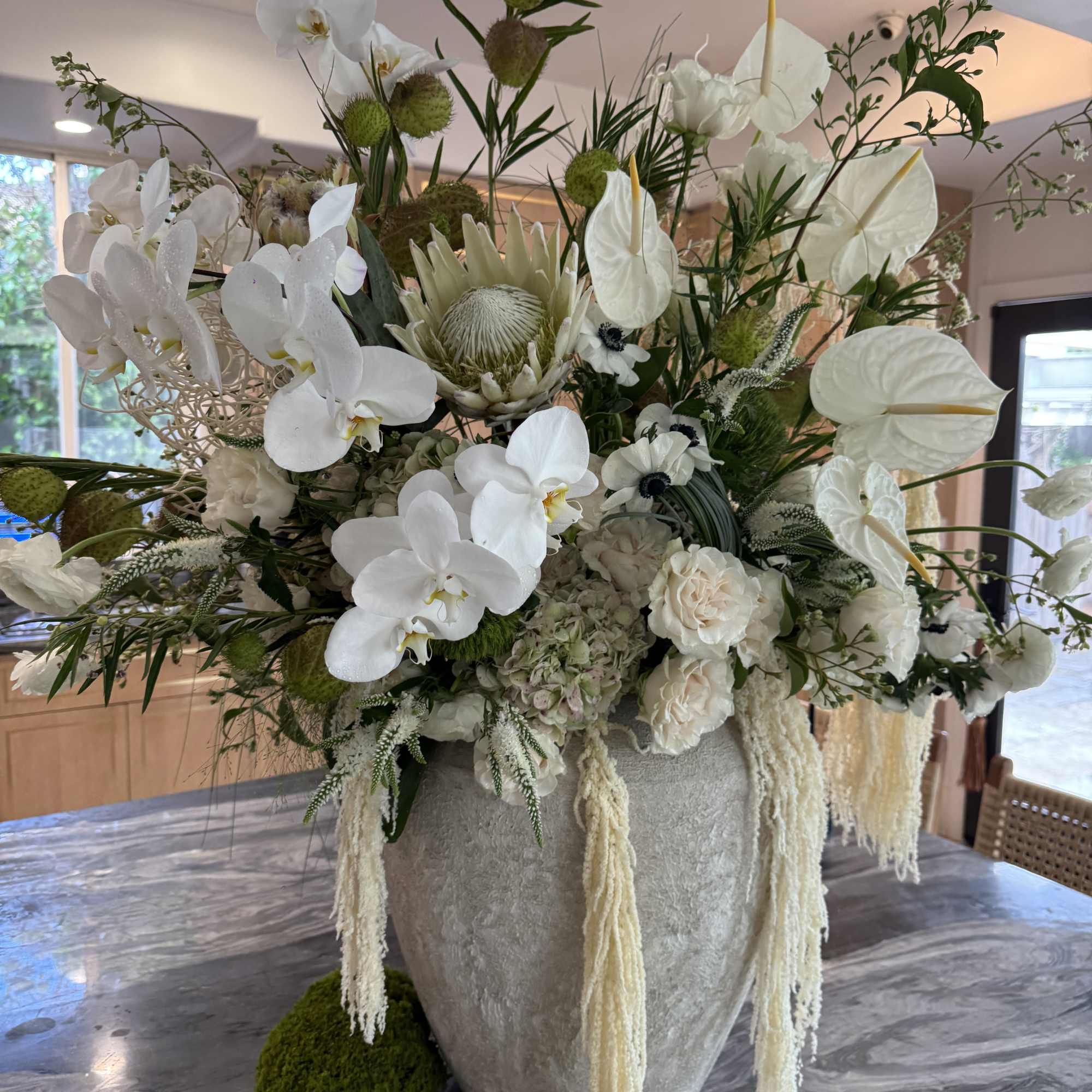 Large white floral arrangement in a textured vase with orchids and anthuriums