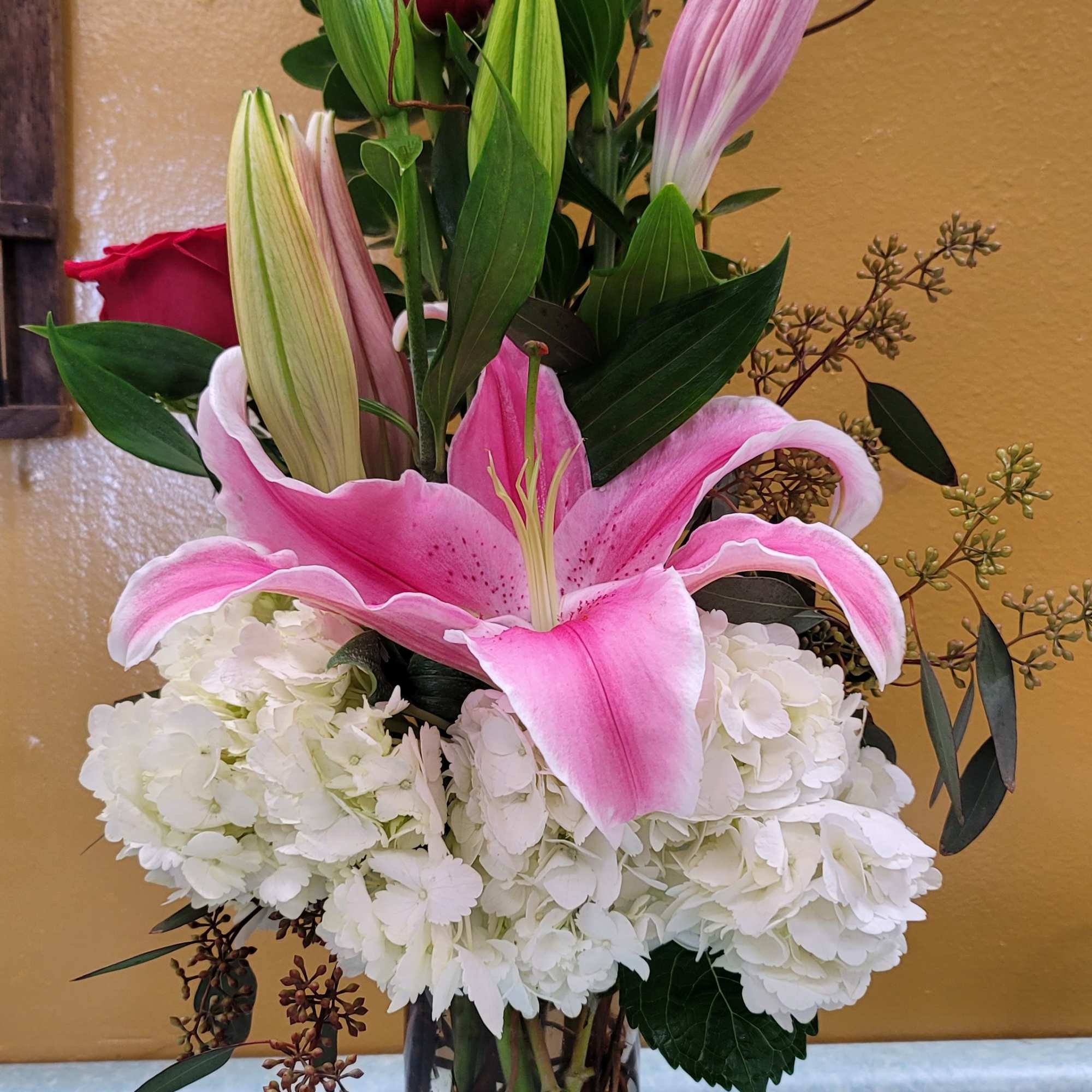 Pink lily and red rose arrangement in a clear glass vase