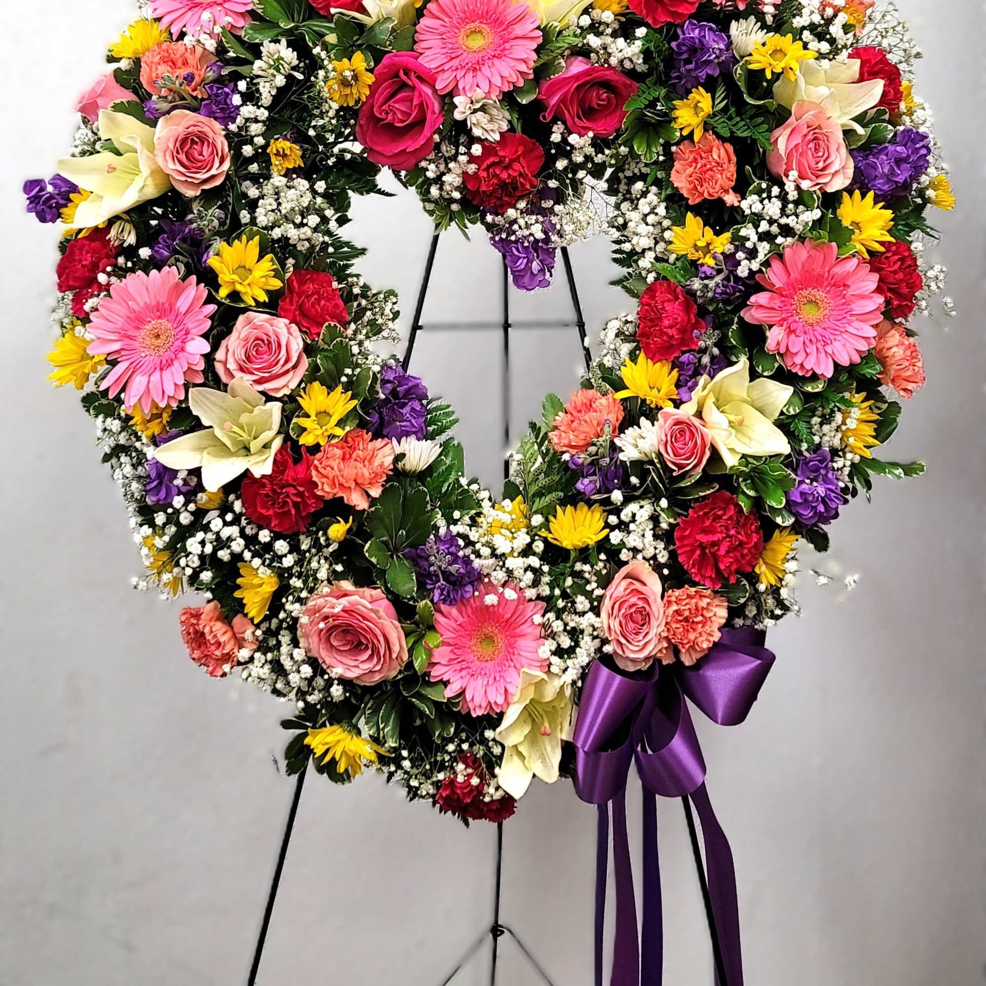 Heart-shaped floral wreath with pink, red, yellow, and white flowers on a stand, photo 2 of 2