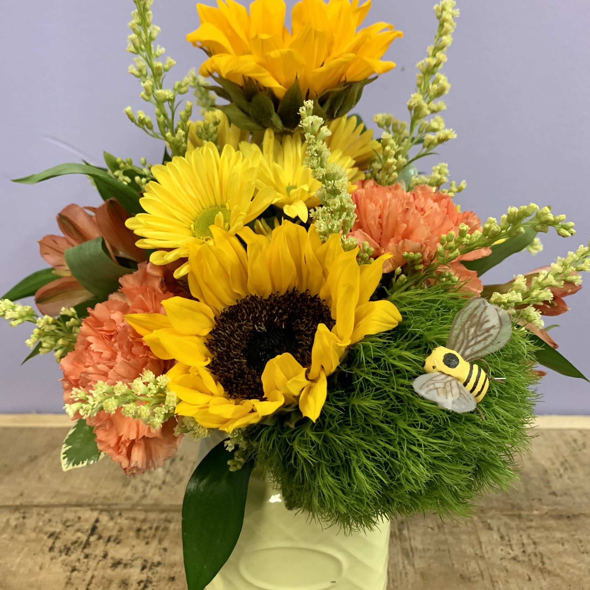 Sunflower and carnation arrangement in a white vase with a bee decoration