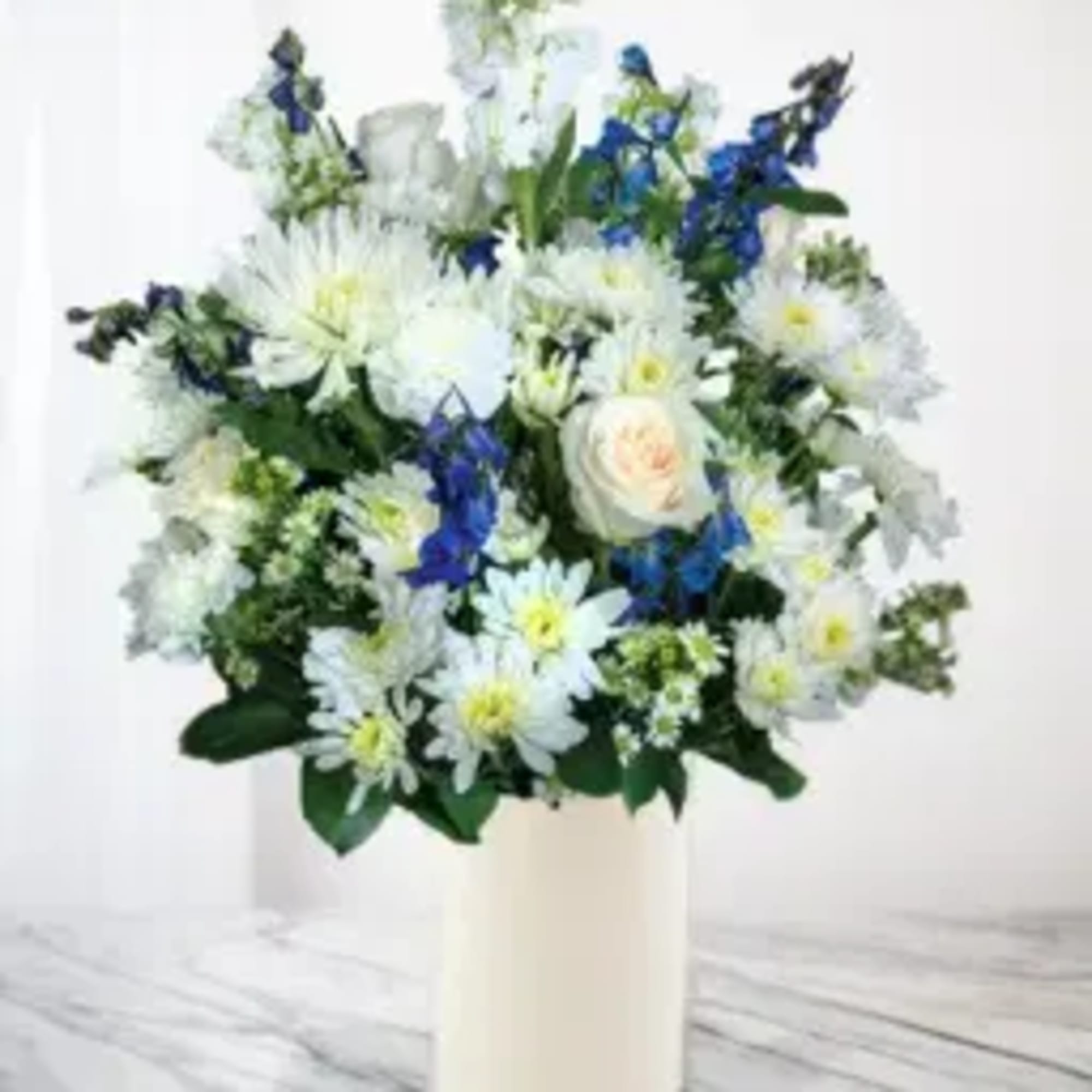 White and blue mixed flower arrangement in a cream vase