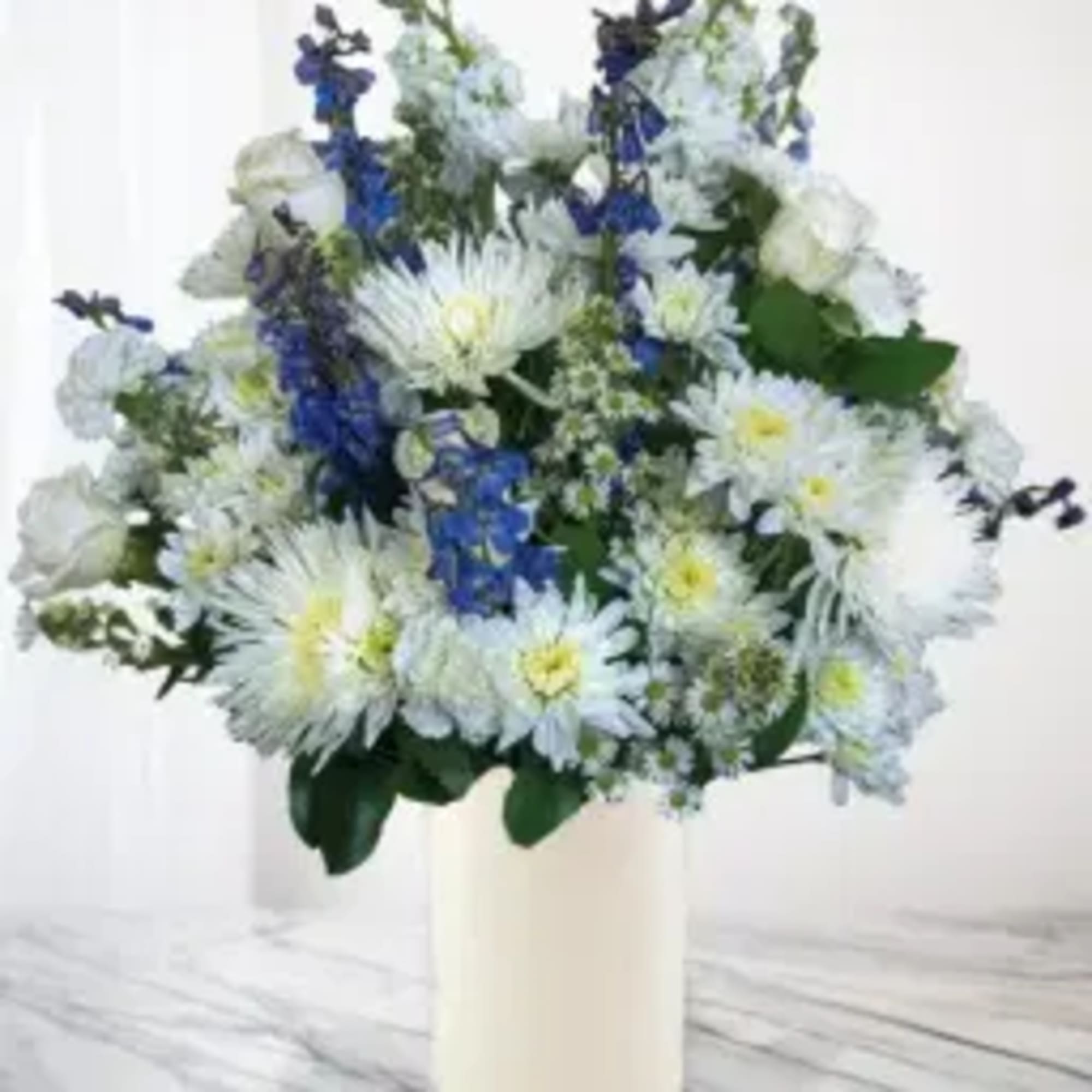 White and blue mixed flower arrangement in a cream vase