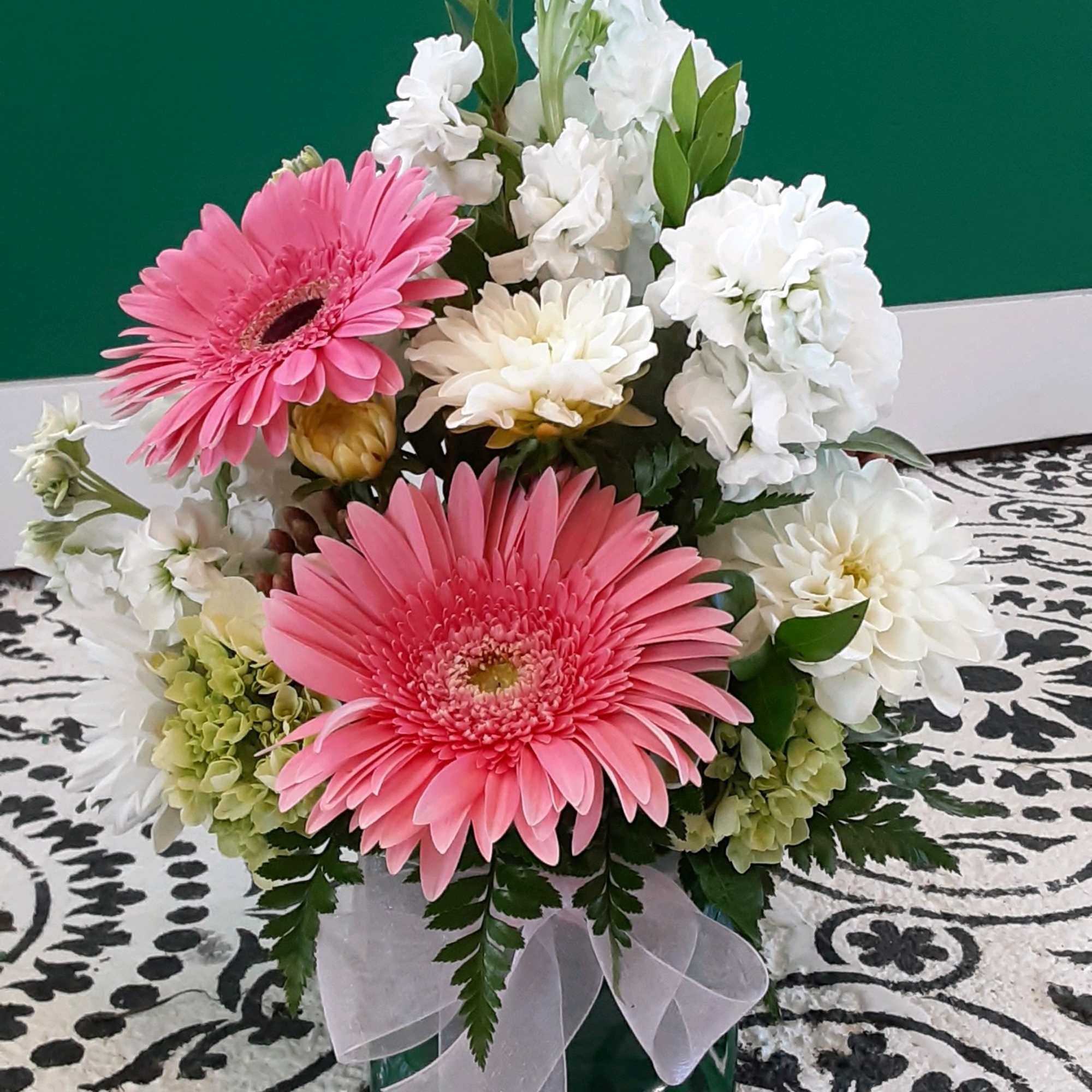 Pink gerbera daisies and white flowers in a glass vase with a ribbon