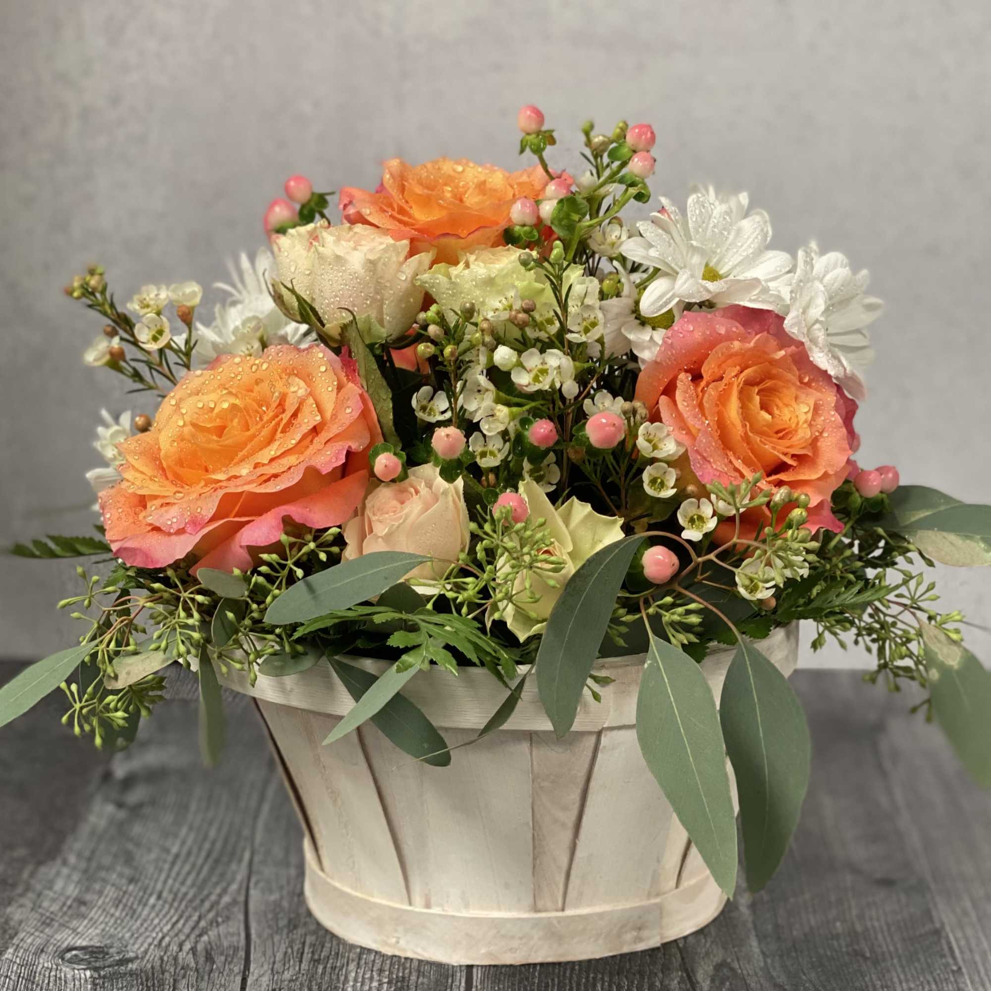 Mixed bouquet of orange and white roses in a pale basket