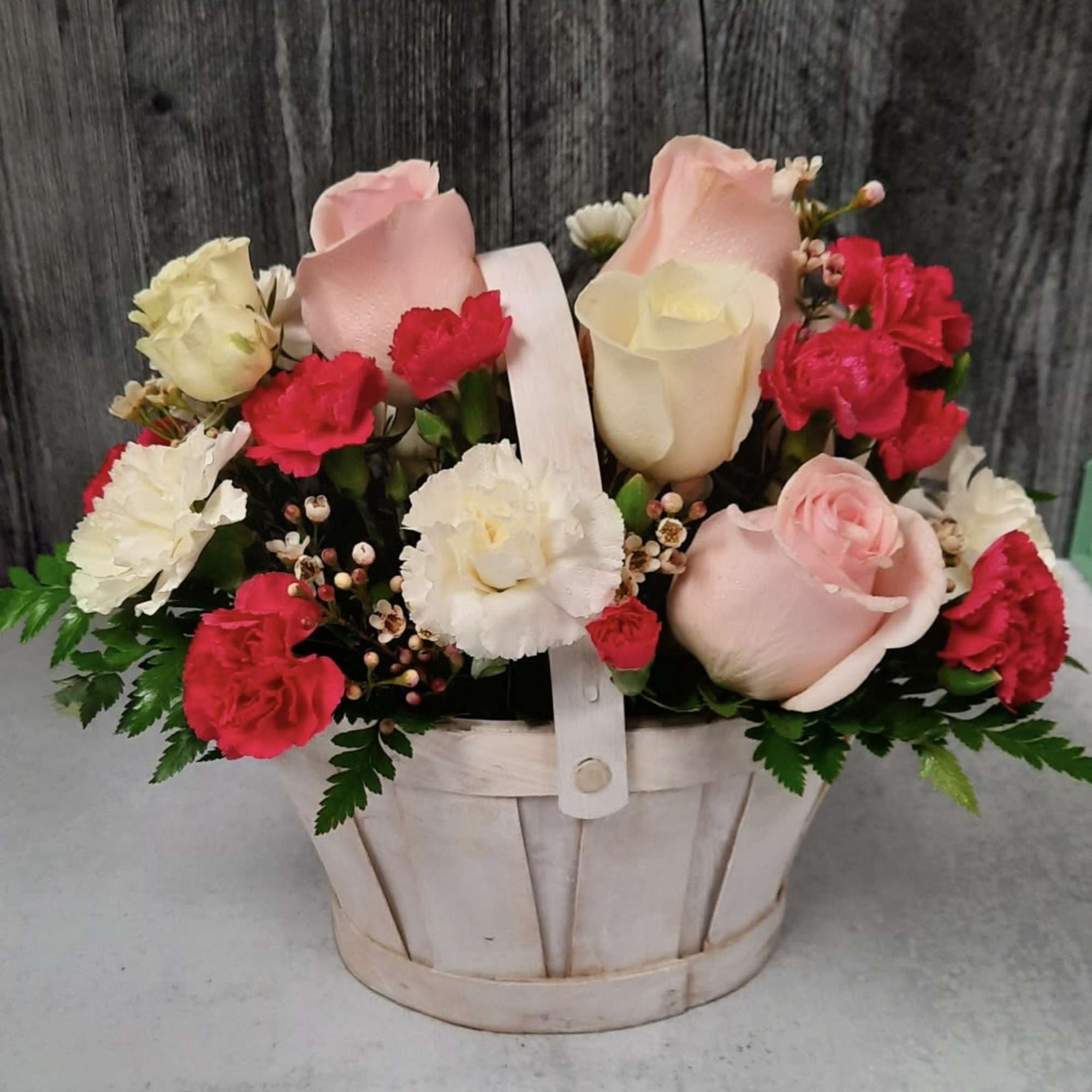 Basket arrangement of pink and white roses with red carnations