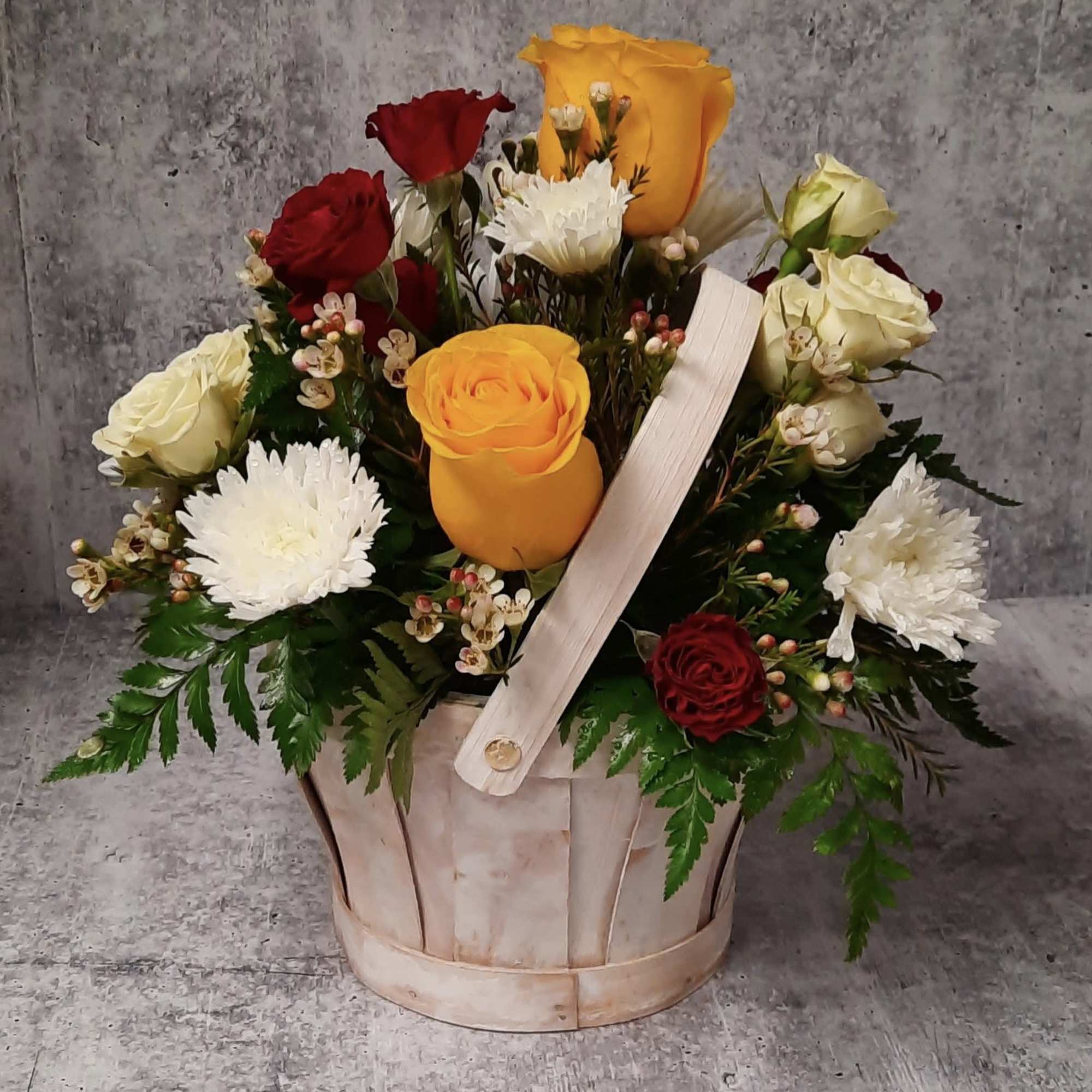 Basket arrangement of red, yellow, and white roses with white mums