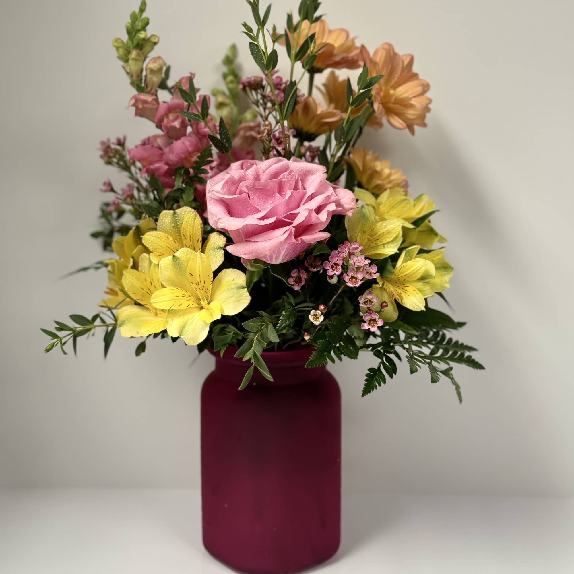 Pink rose and yellow flower arrangement in a magenta vase