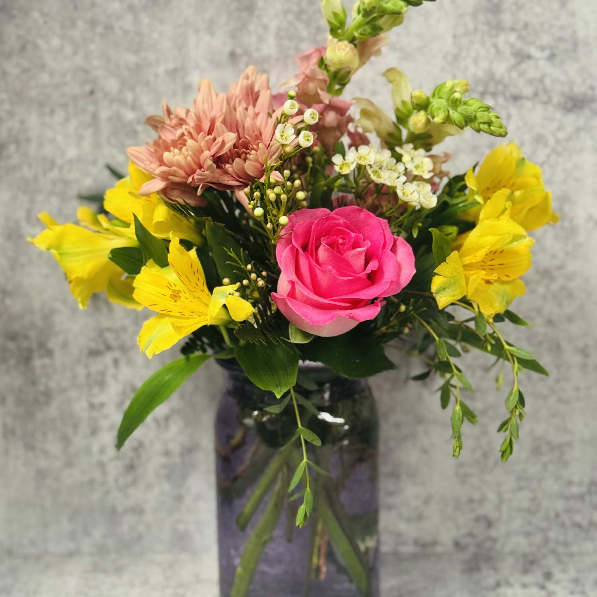 Pink rose and yellow flower arrangement in a dark glass vase