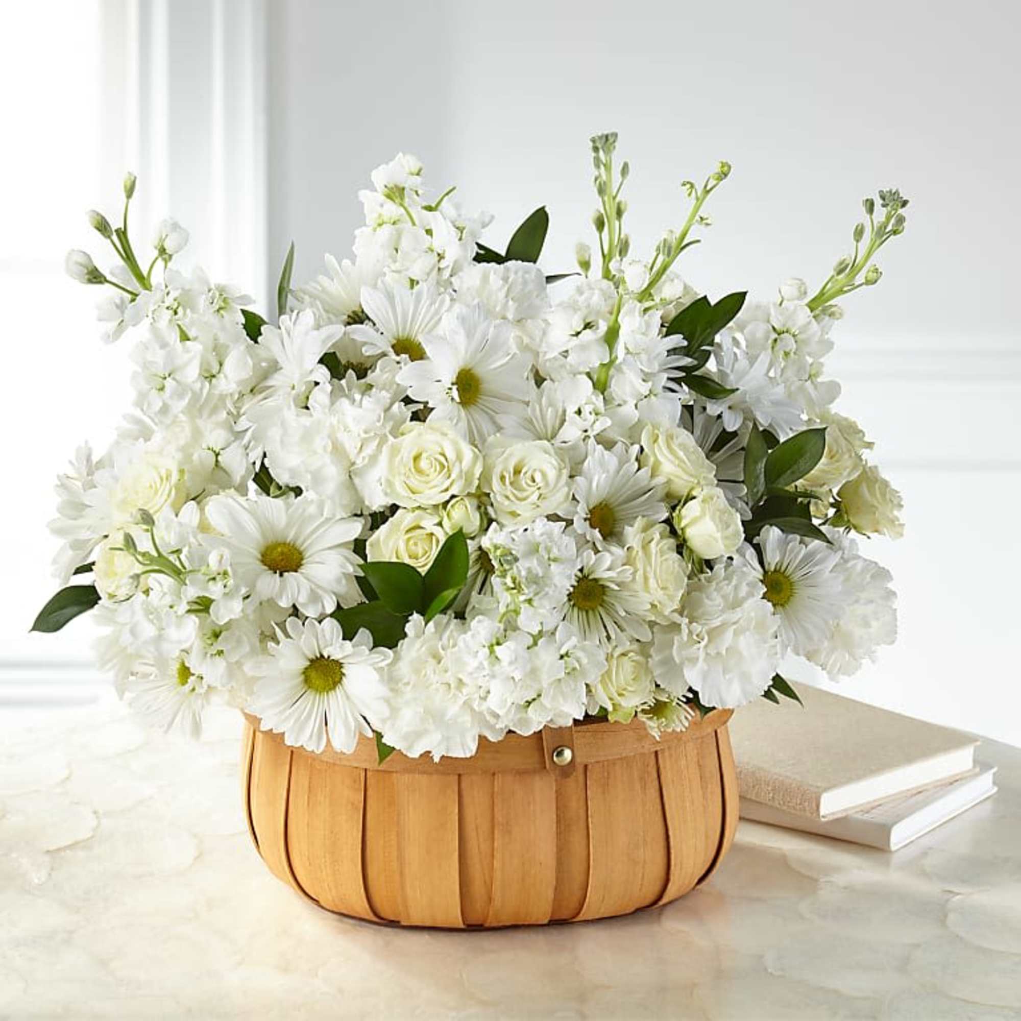 White flowers arranged in a wooden basket with books beside it