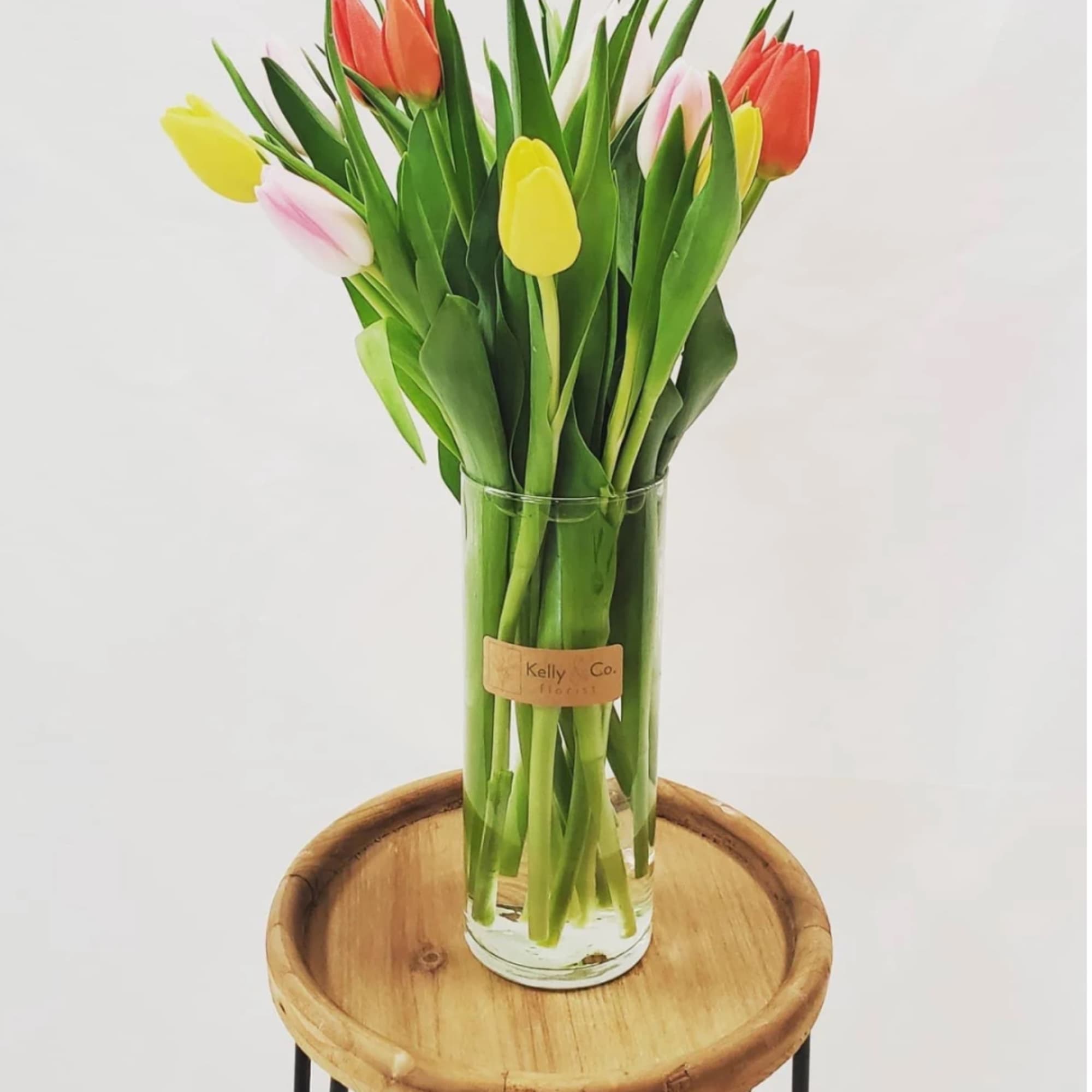 Glass vase of colorful tulips on a wooden stand