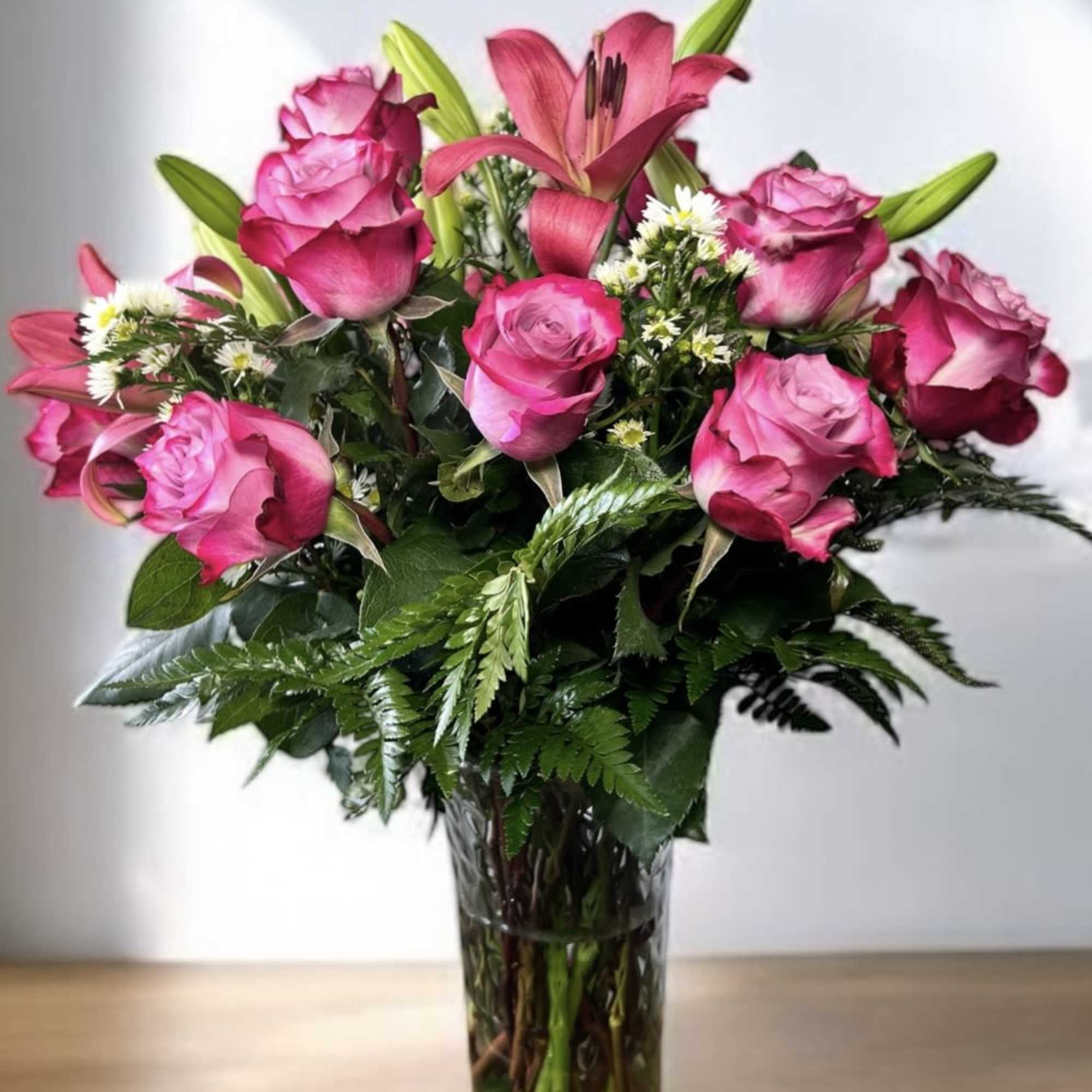 Pink roses and a lily arranged in a clear glass vase