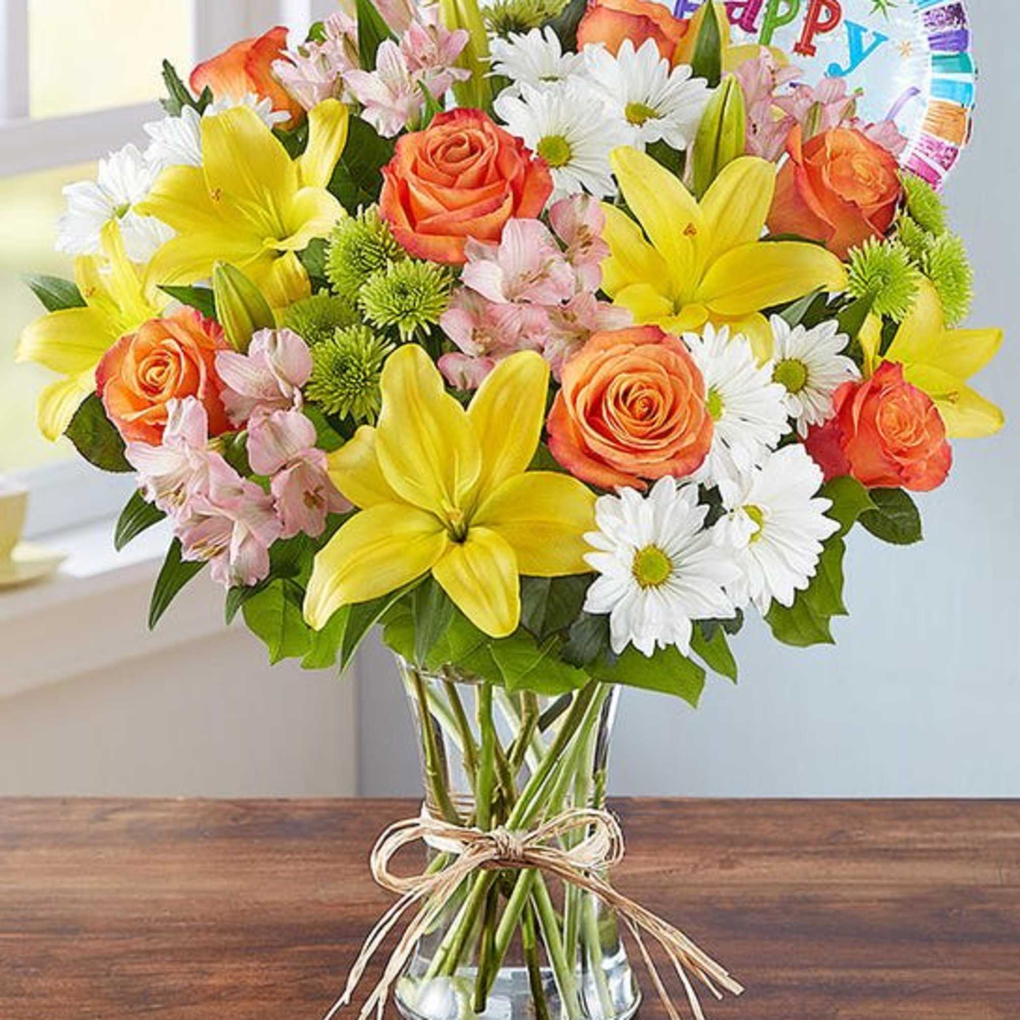Bouquet of yellow lilies, orange roses, and white daisies in a glass vase
