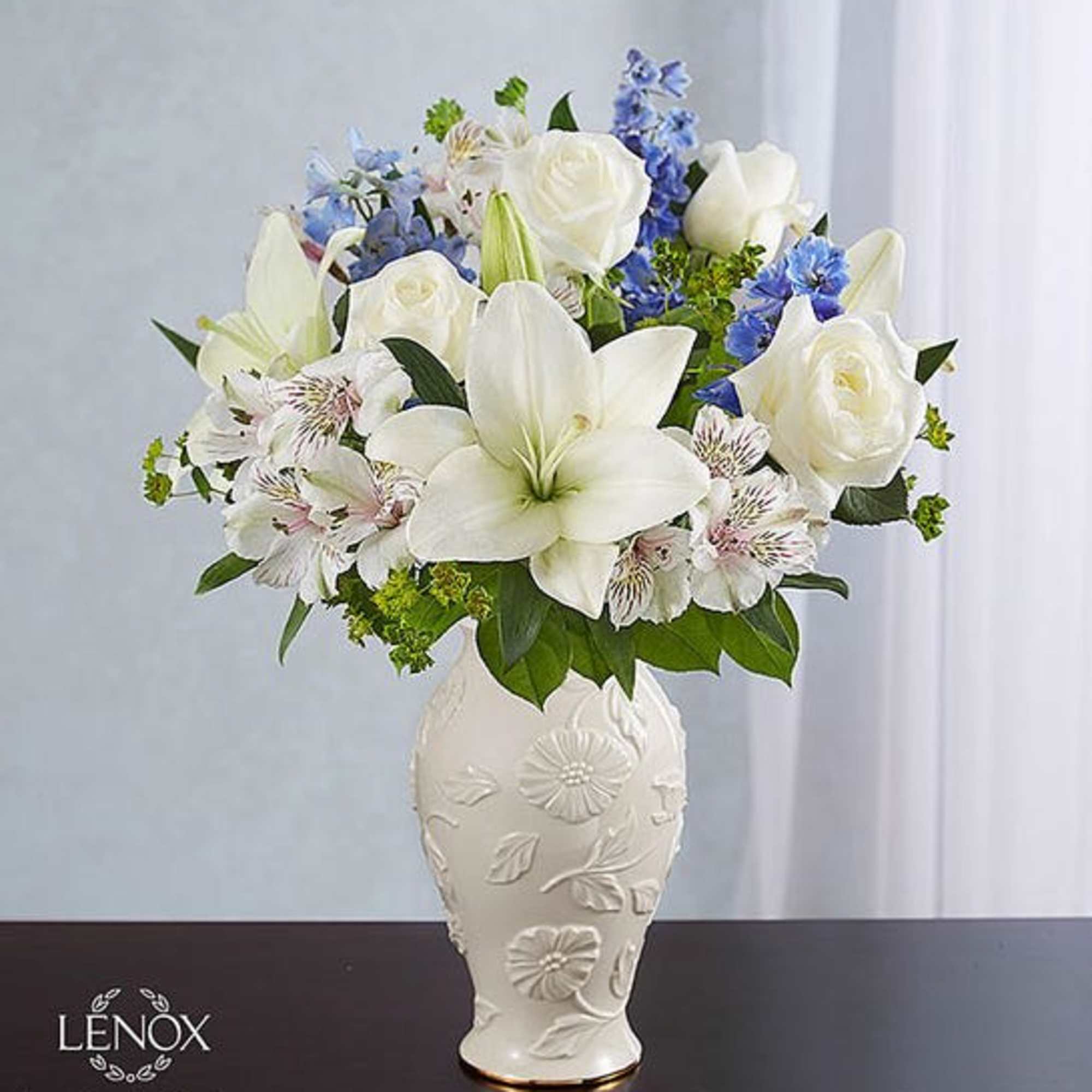 White lilies and roses arranged in a decorative vase with blue accents
