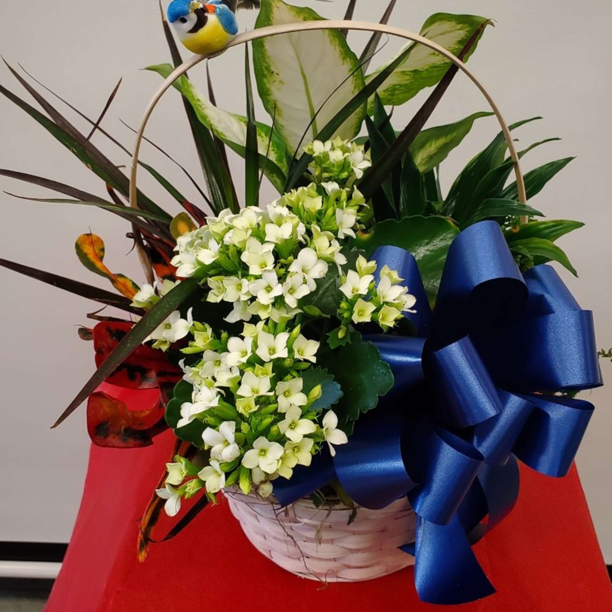White flowers in a basket with a large blue ribbon and decorative bird