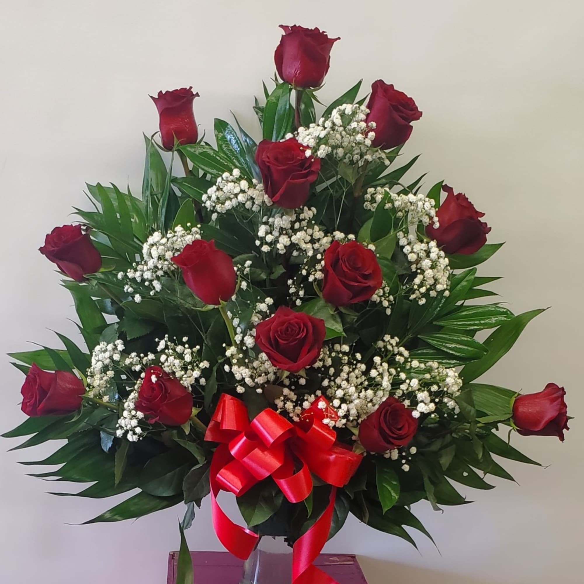 Red roses arranged in a vase with baby's breath and a red ribbon