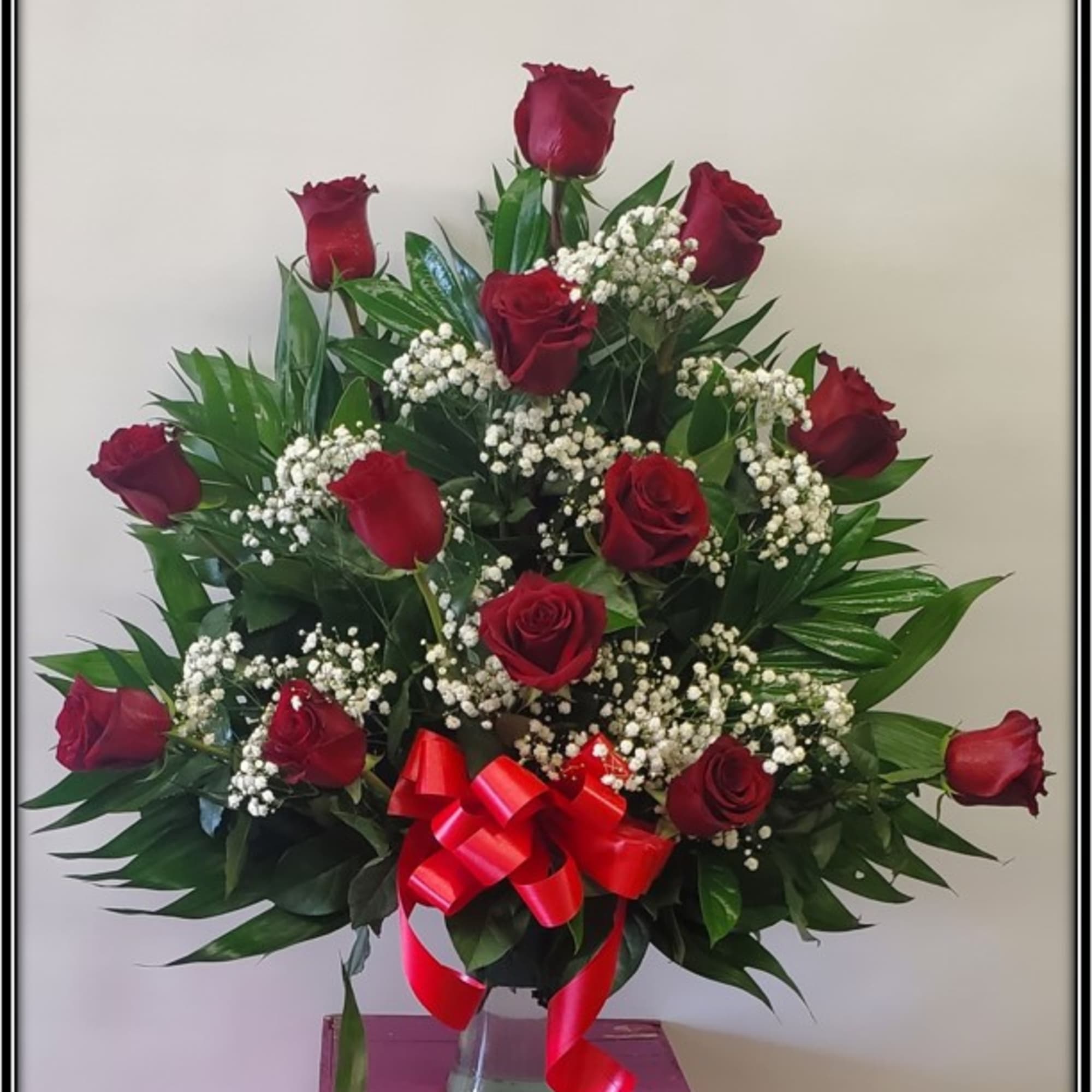 Red roses arranged in a clear vase with baby's breath and a red ribbon