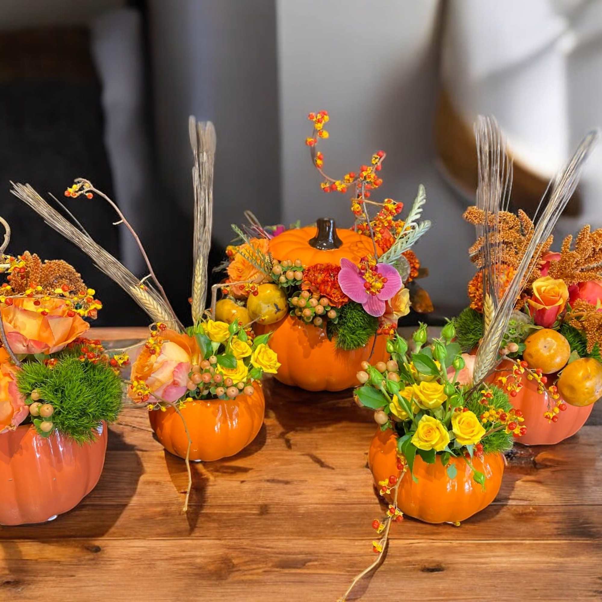 Mini pumpkin arrangements with orange and yellow flowers on a wooden table