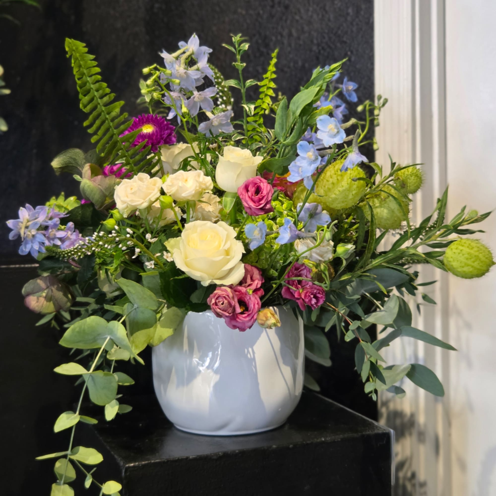 Mixed bouquet of roses, blue flowers, and greenery in a white vase