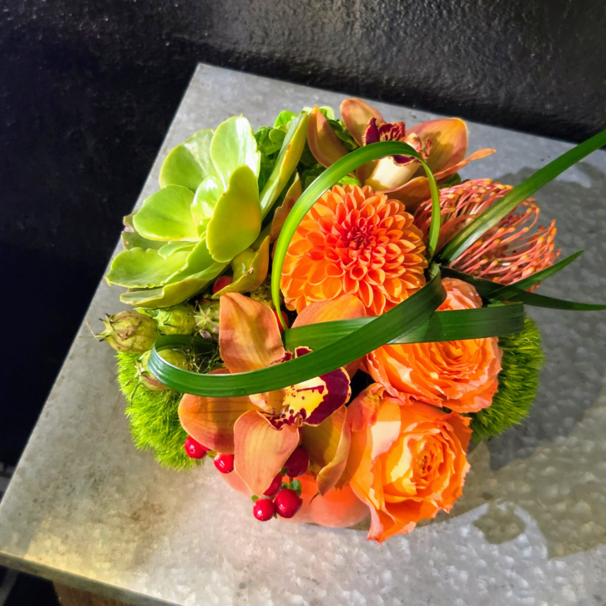 Orange floral arrangement with orchids and a dahlia in a low container
