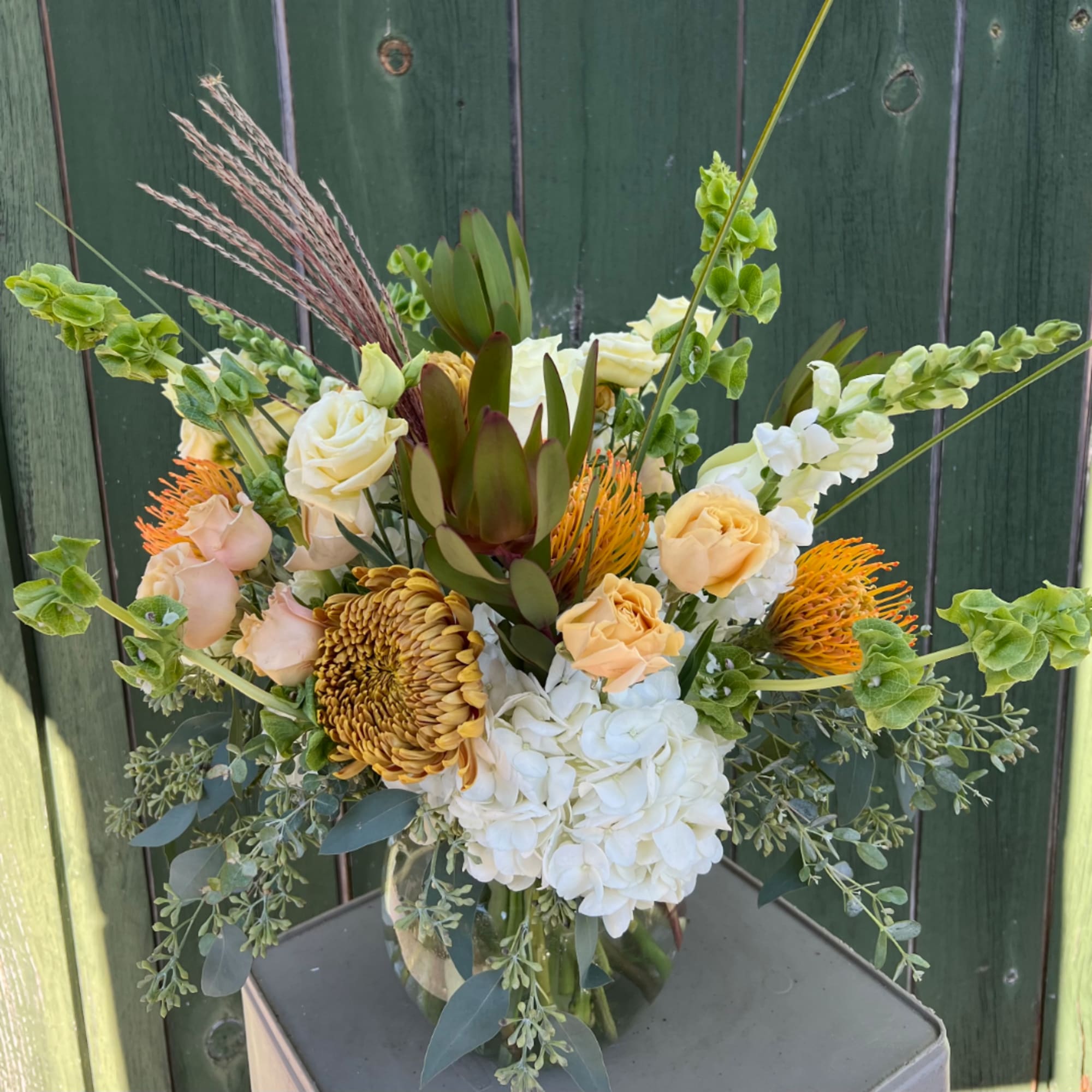 Mixed bouquet with white hydrangea, peach roses, and orange blooms in a glass vase