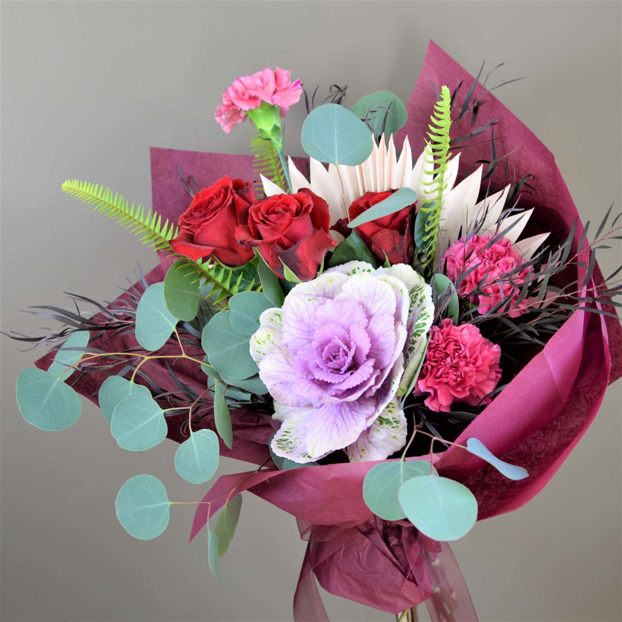 Bouquet of red roses, pink carnations, and a lavender ornamental cabbage