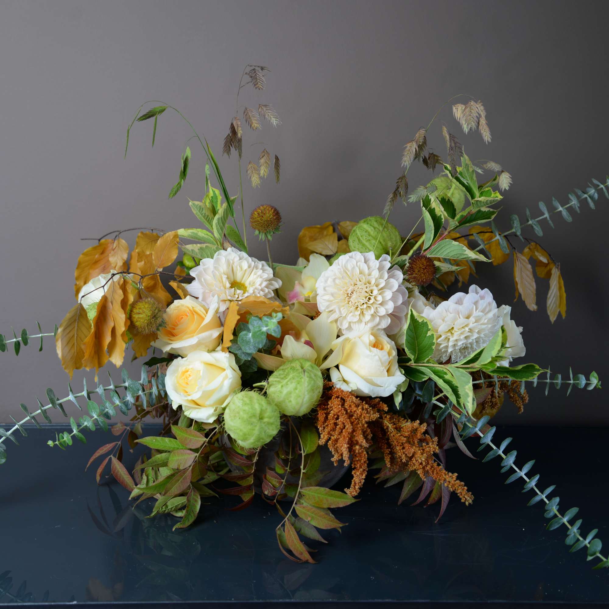 Arrangement of white and pale yellow flowers with autumn foliage
