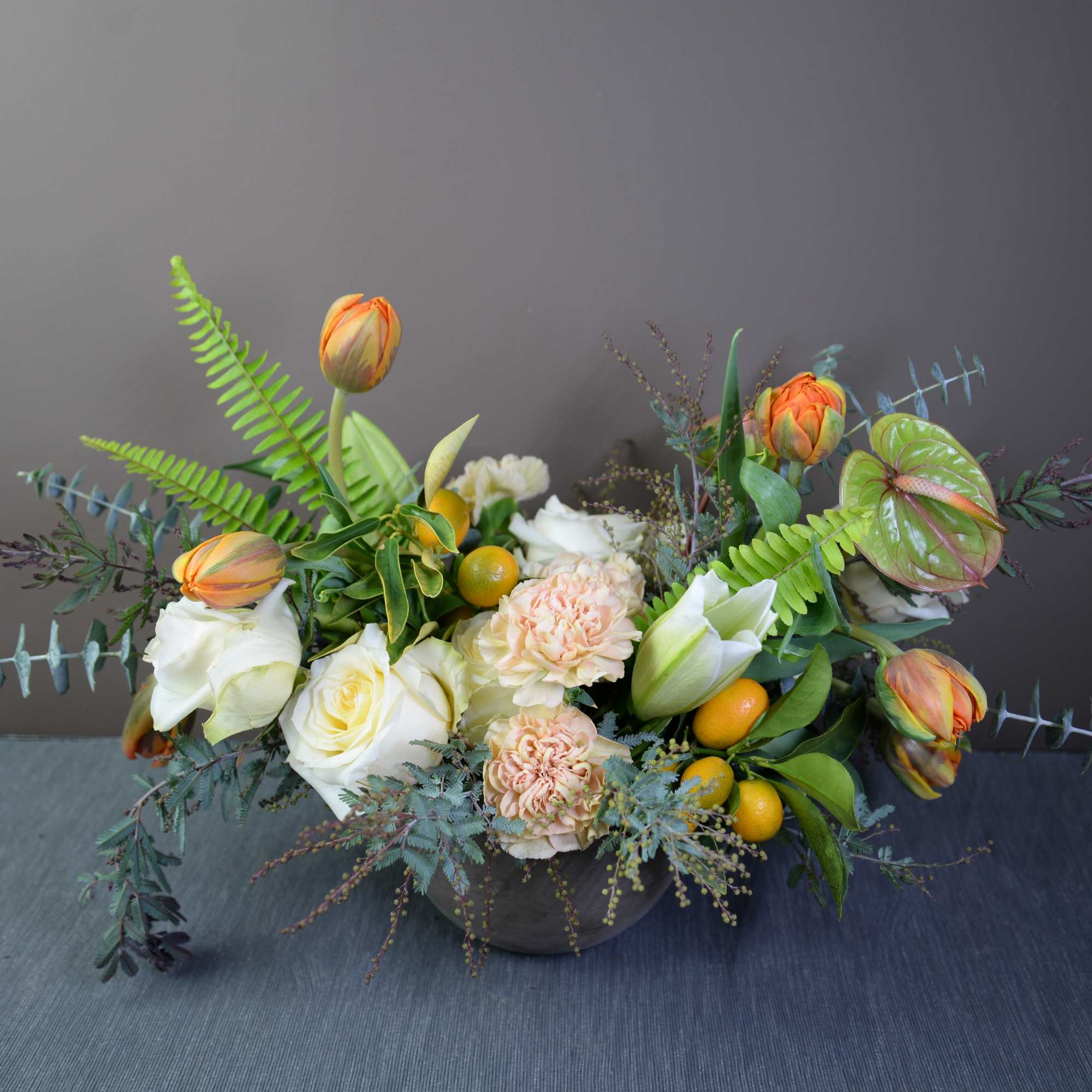 Low floral arrangement with white roses, peach blooms, and orange tulips in a bowl vase
