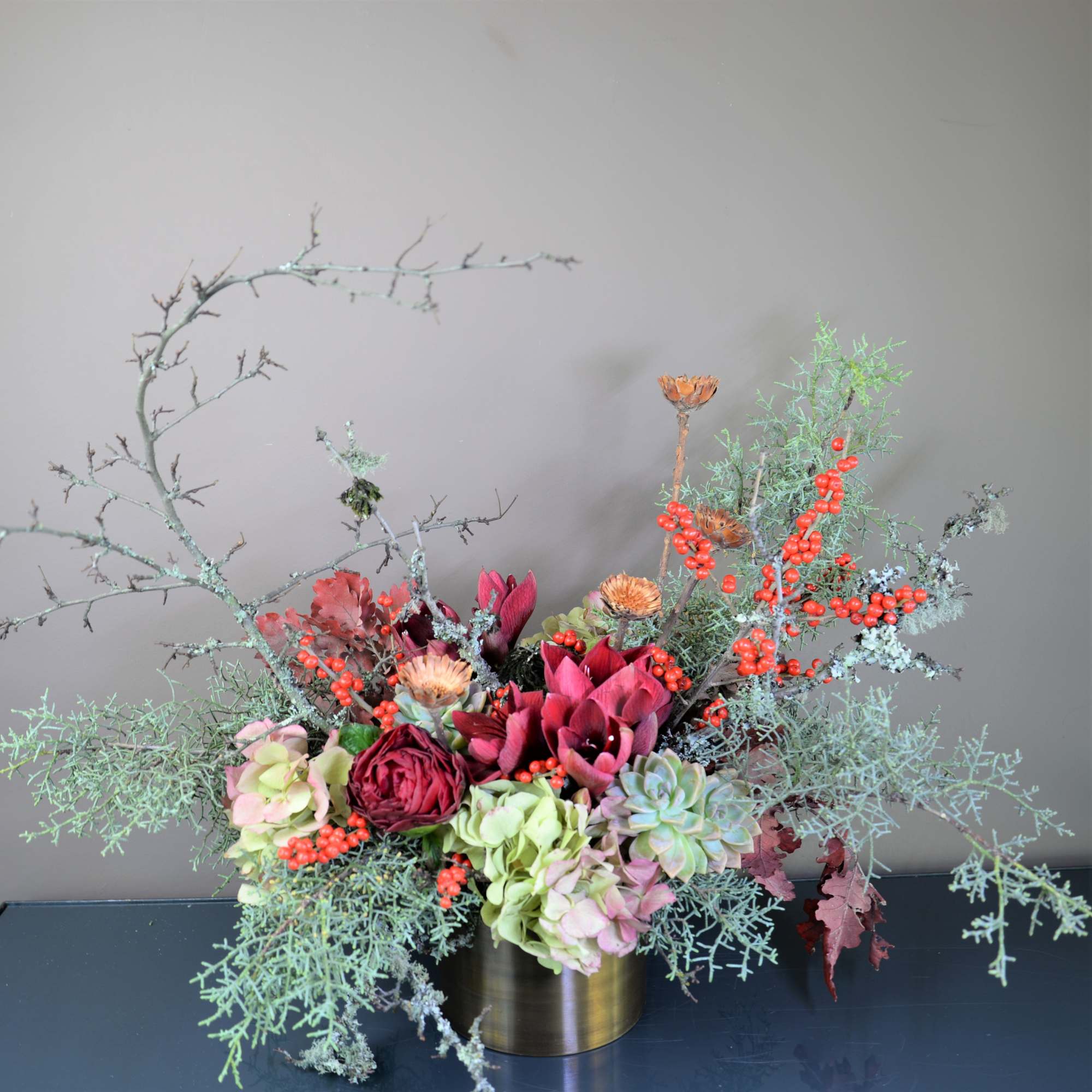 Mixed floral arrangement in a gold vase with red blooms and berries