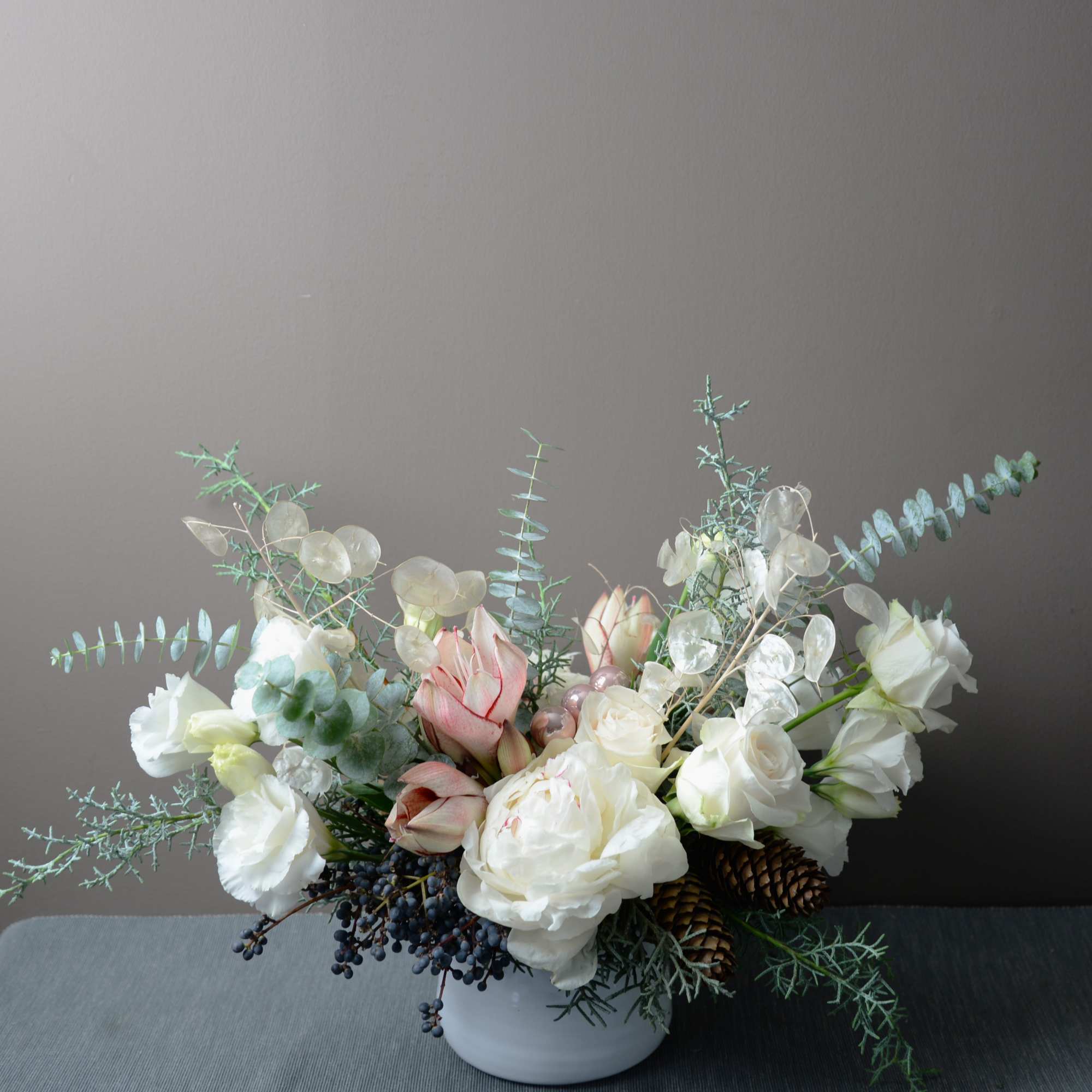 White and blush flowers arranged in a low white vase with pinecones and airy branches.
