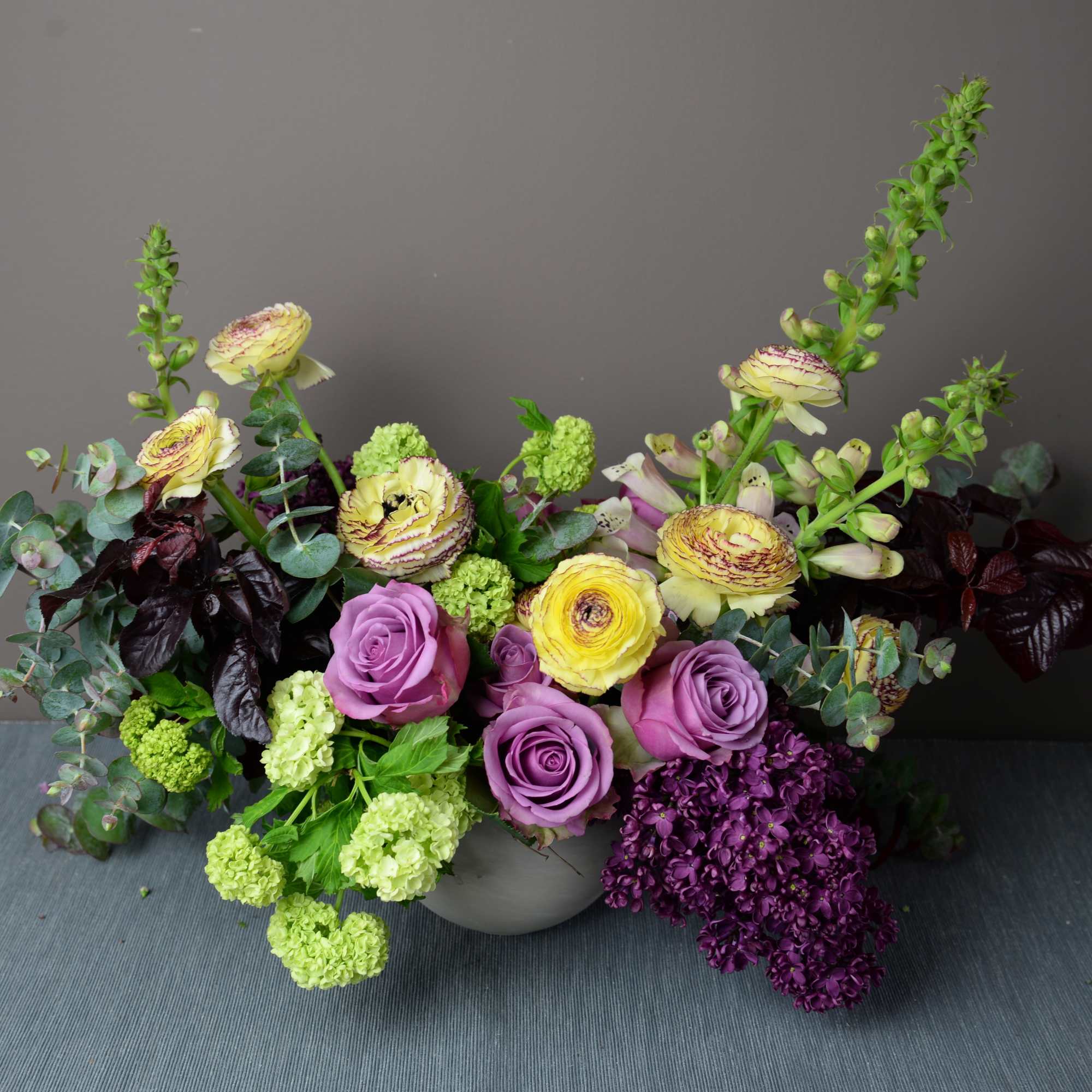 Mixed bouquet of purple roses, green blooms, and tall yellow flowers in a vase