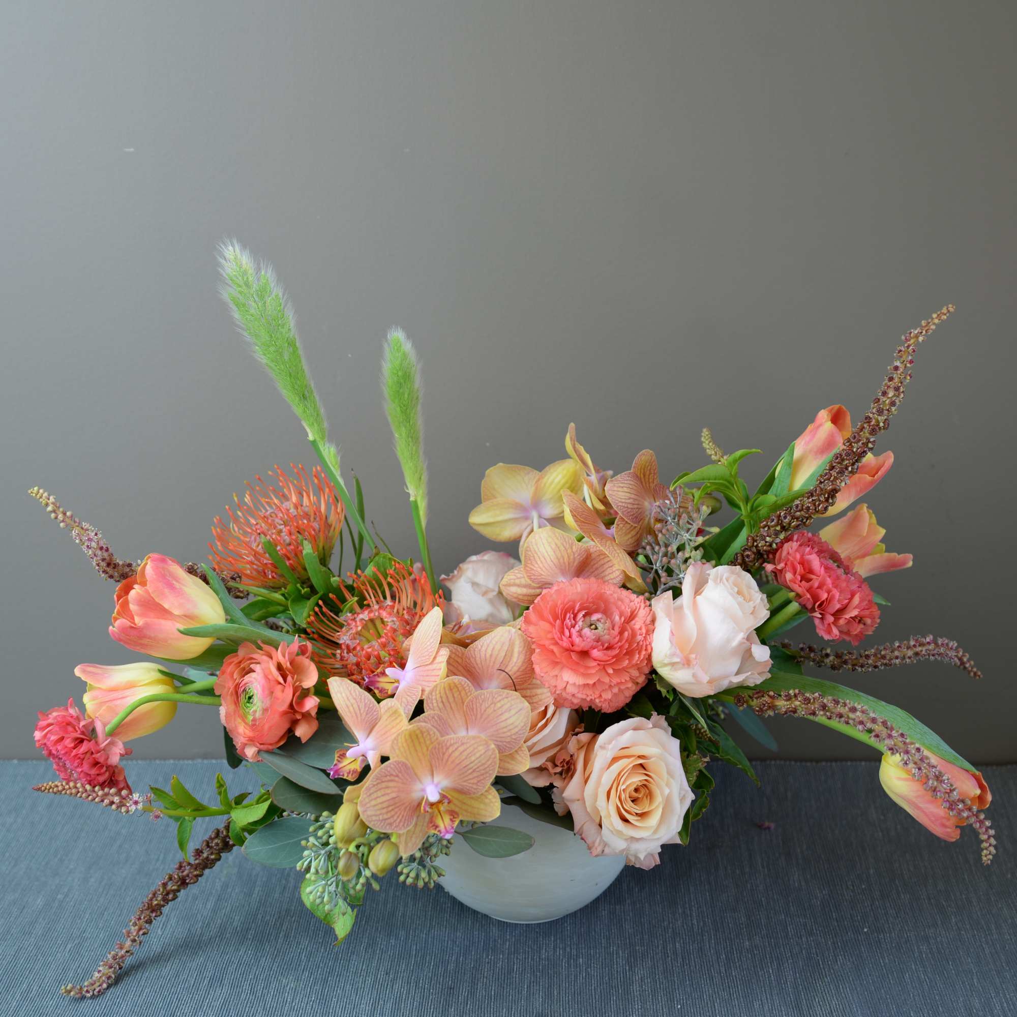 Low floral arrangement in a white bowl with peach, pink, and orange blooms