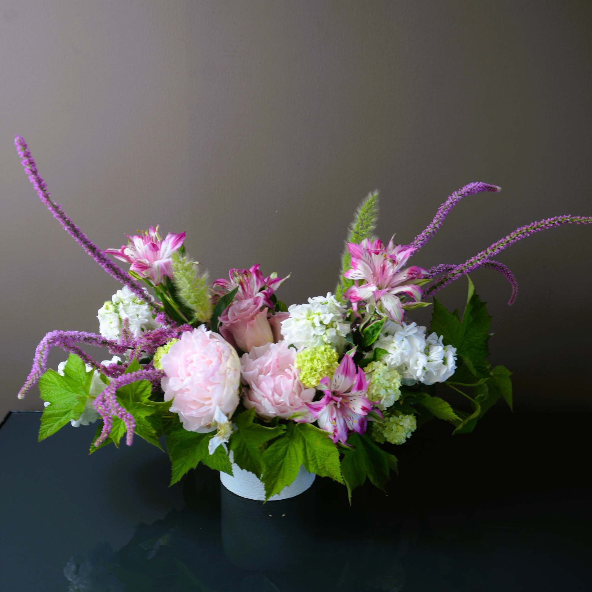 Pink and white floral arrangement in a white container with purple accents