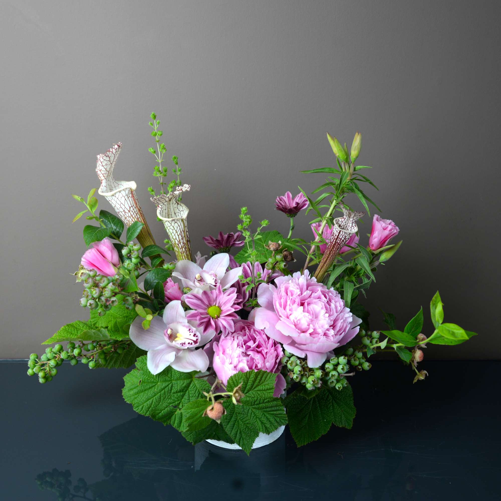 Pink and white floral arrangement with orchids and peonies in a low container