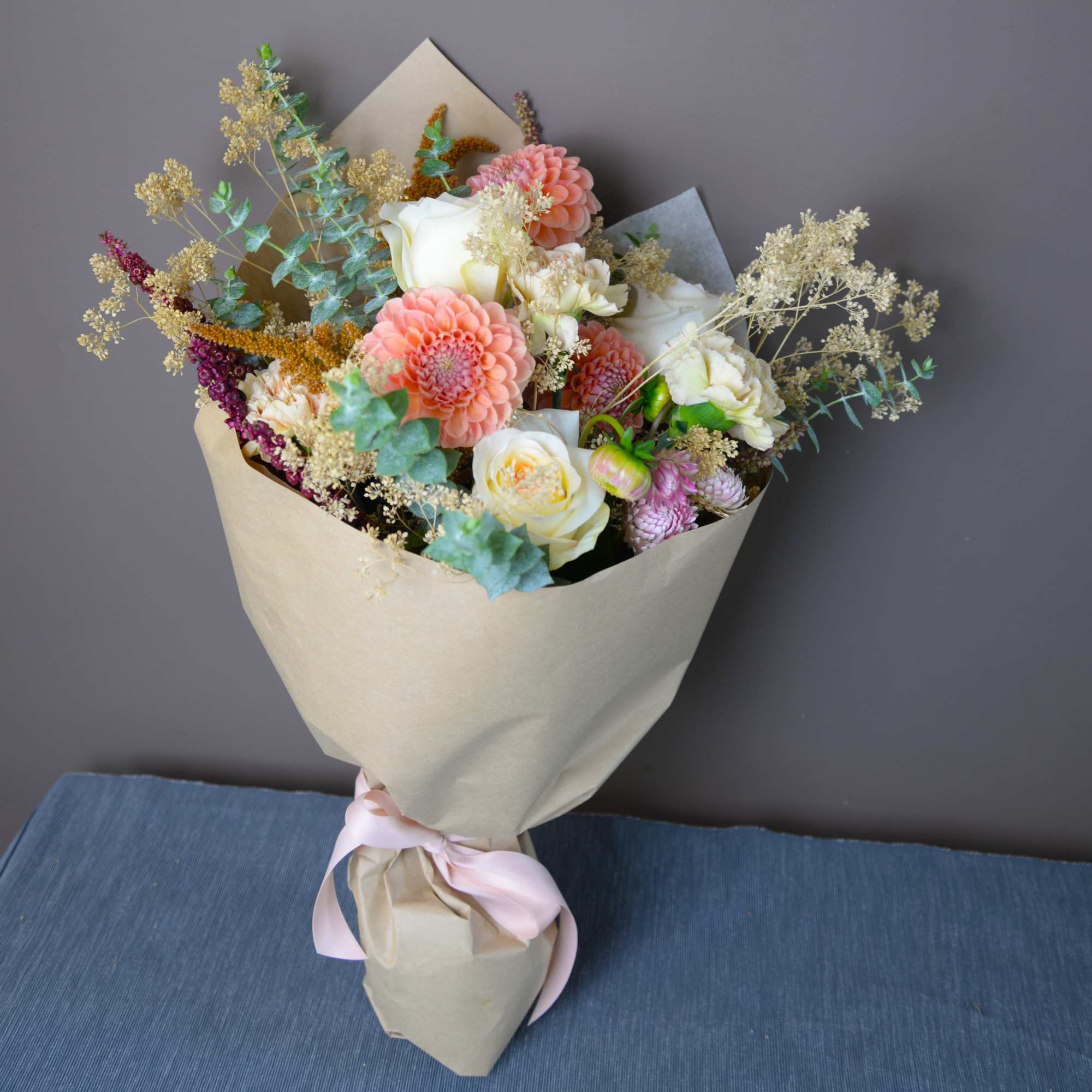 Hand-tied bouquet of white and peach flowers wrapped in kraft paper