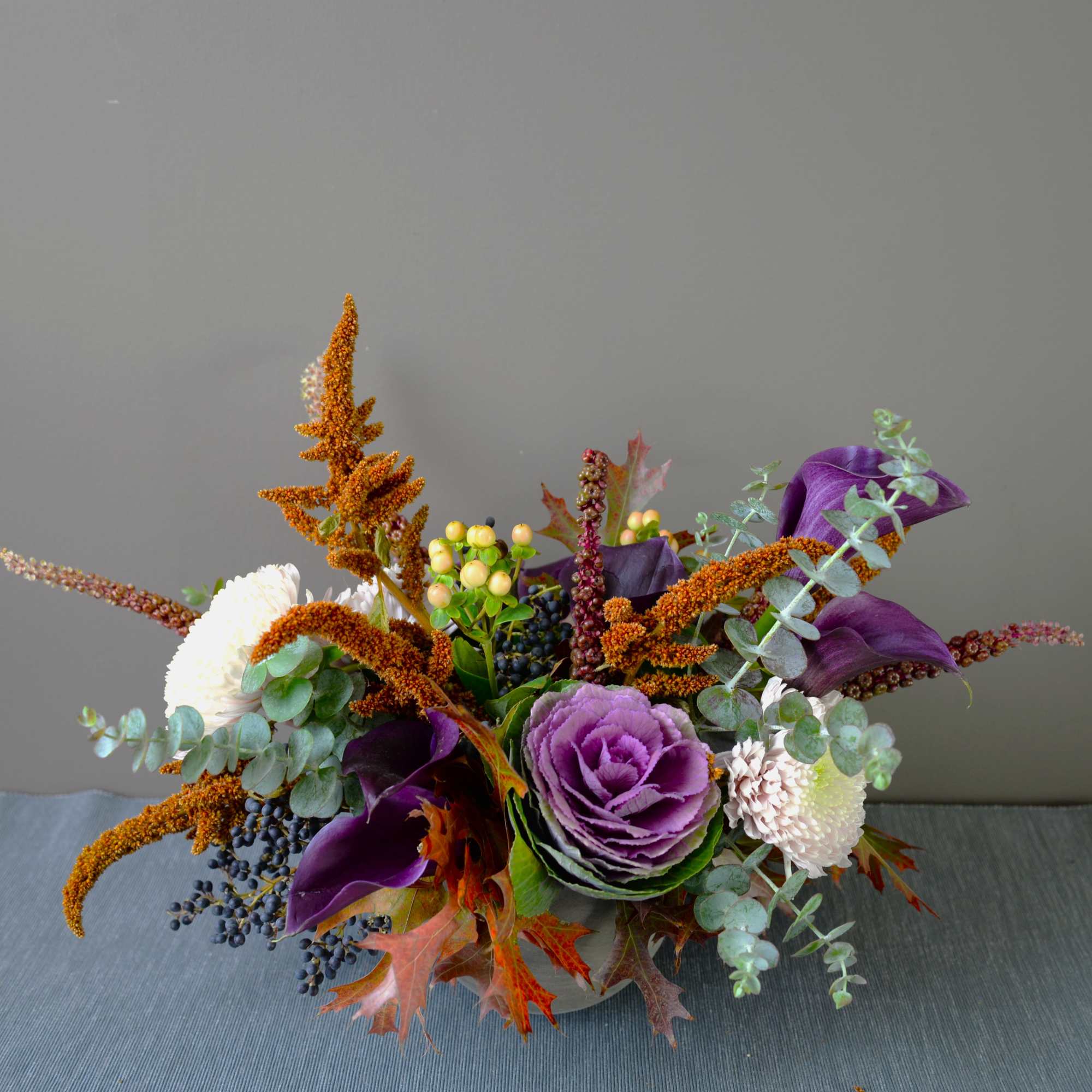 Purple and white floral arrangement with orange accents in a low container