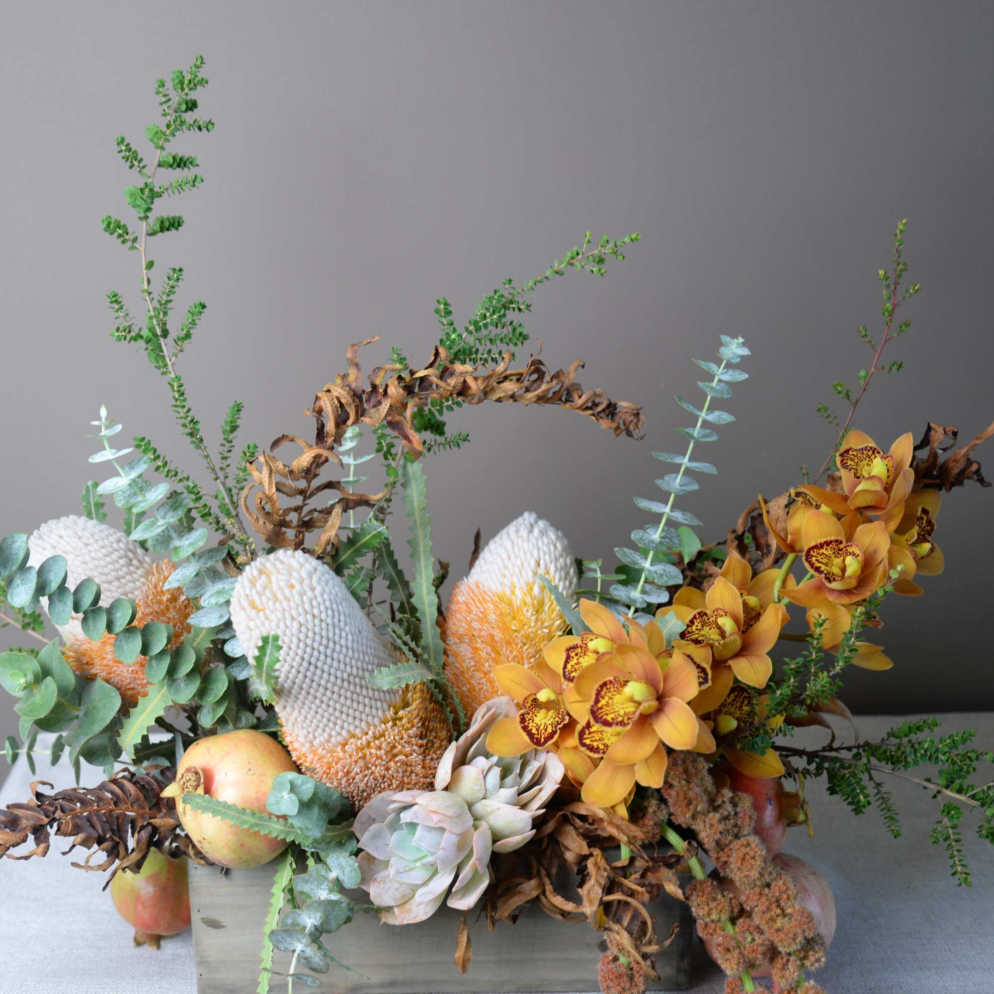 Mixed floral arrangement with orange orchids, succulents, and apples in a low container