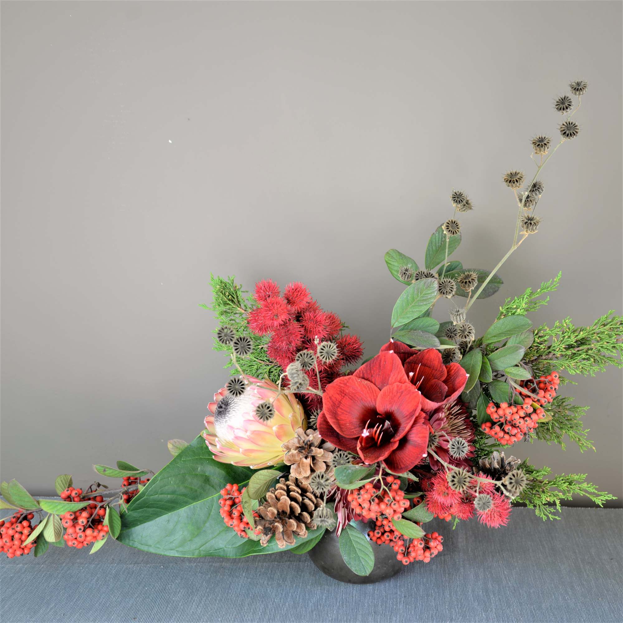 Red and pink floral arrangement in a low black container with berries and pinecones