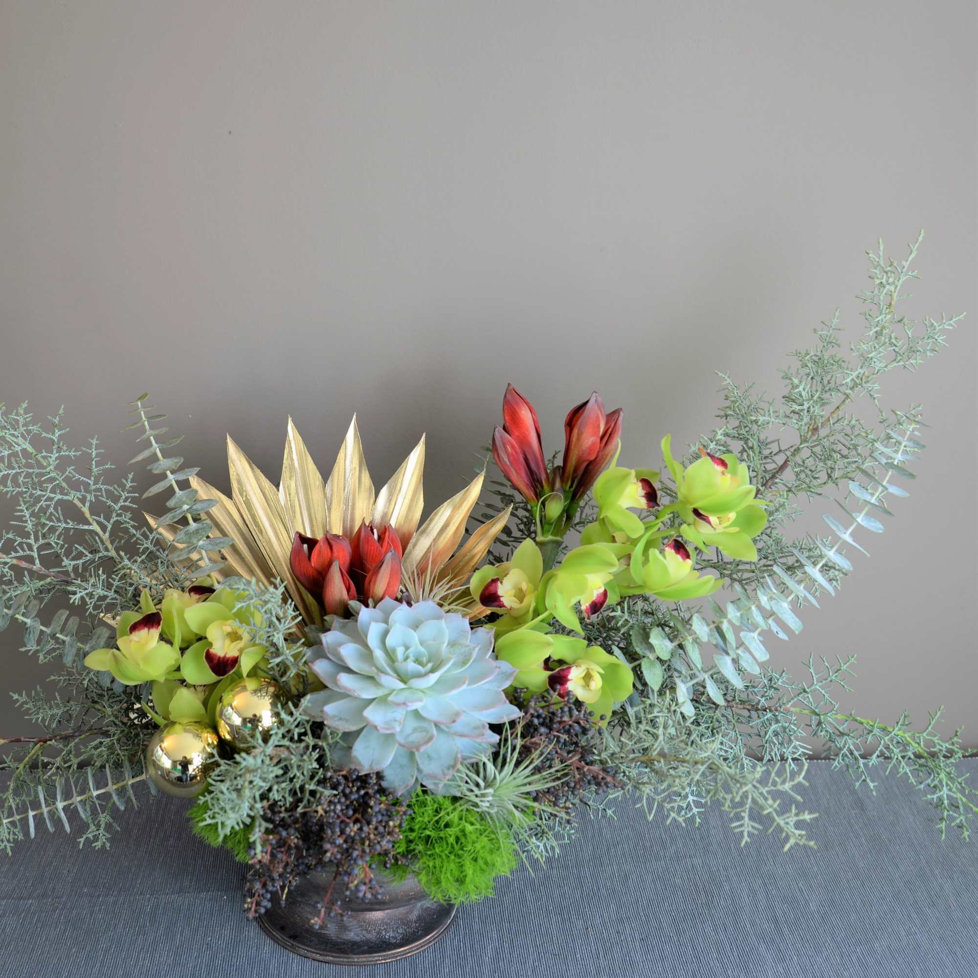 Succulent arrangement with green orchids and red blooms in a low container