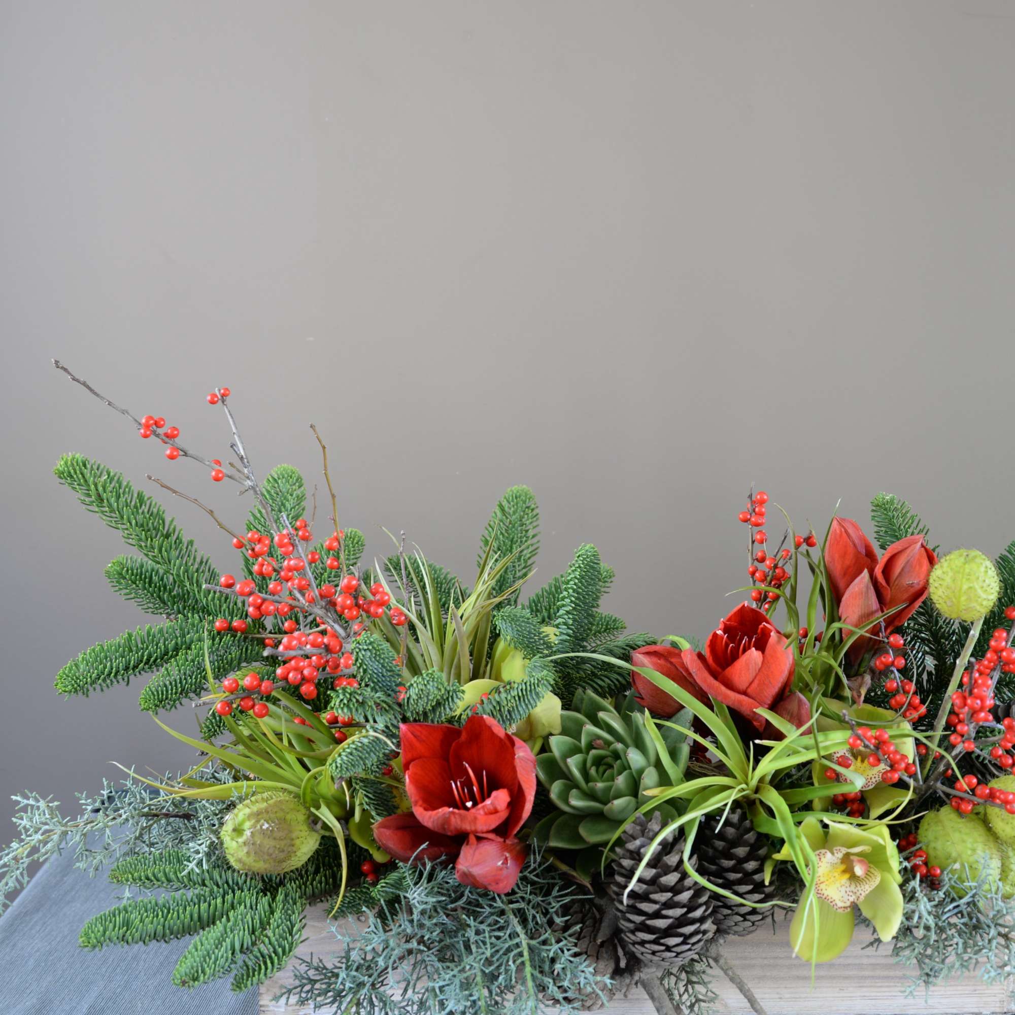 Holiday arrangement with red flowers, berries, pinecones, and succulents